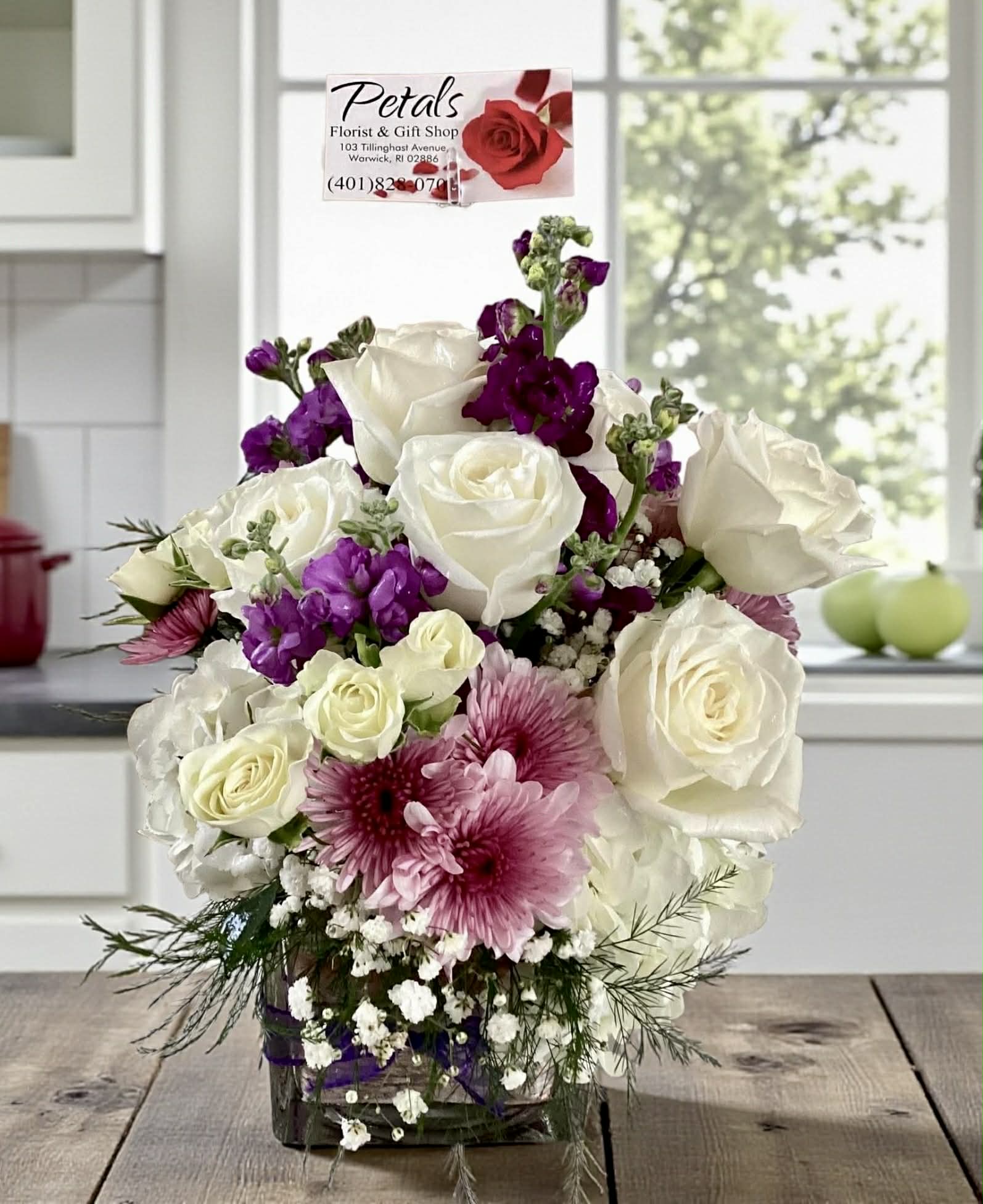 Simply Chic Cube by Petals - Conveying a sense of luxury and elegance, this arrangement is a truly majestic display. It highlights minimalist elegance with a sophisticated palette. This design features premium white roses, white spray roses, and fluffy mounds of white hydrangeas, beautifully contrasted with fragrant purple stock and lavender poms. Accents of classic baby's breath and lush greens complete the look. The entire arrangement is professionally designed in a classic glass cube vase, offering a timeless and chic presentation. It's the perfect statement piece for any home or a thoughtful gift that speaks volumes of refined taste.