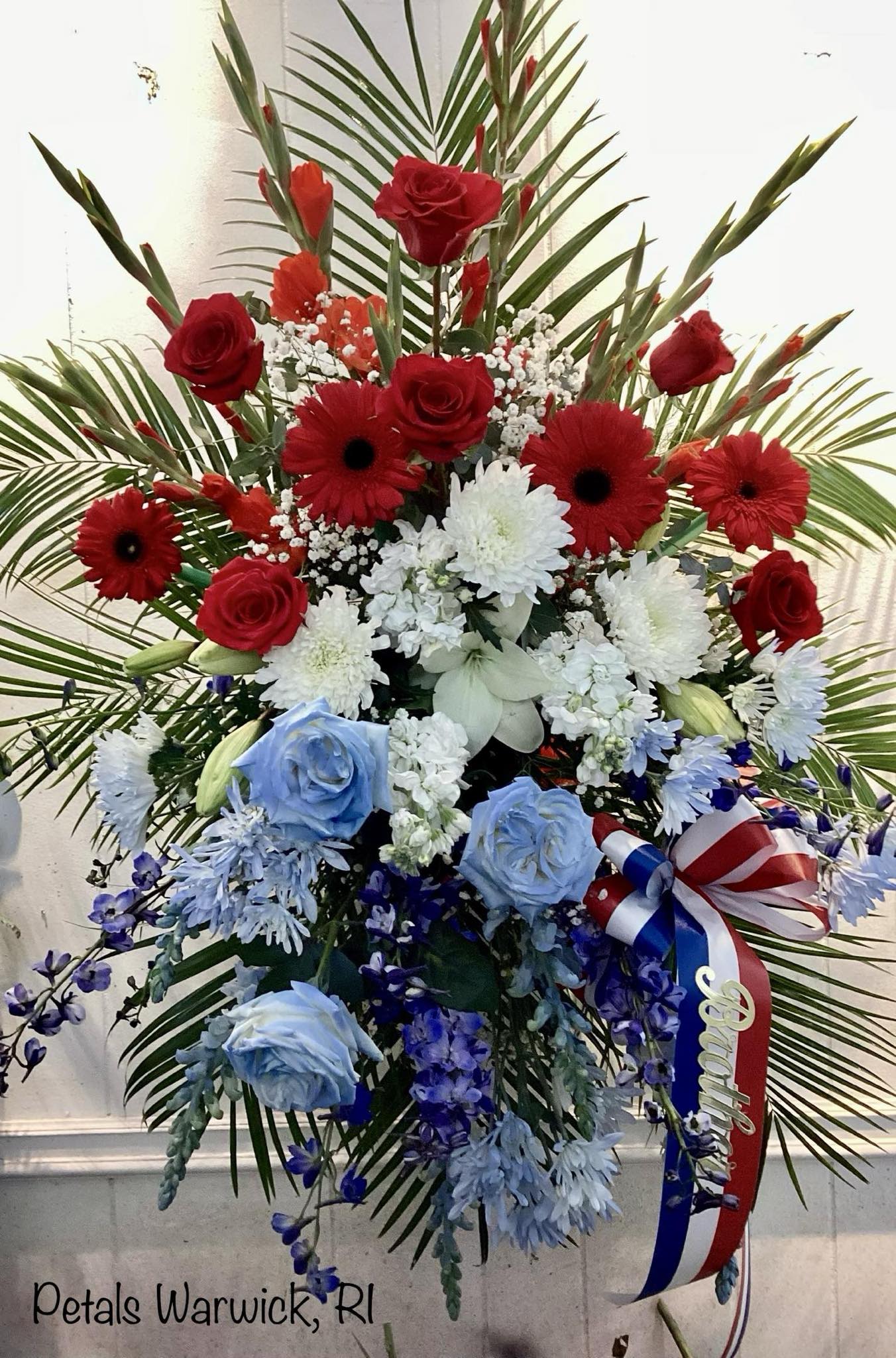 Patriotic Standing Spray Tribute by Petals - Please allow 24 to 48 hours for this design so I can deliver your flower on time. If you need immediate delivery, contact me at 401-828-0701 for a telephone consultation today.   Honor your loved one who proudly served our Nation with a big, beautiful Patriotic Standing Spray Tribute for their celebration of life service. Designed with a beautiful array of Red, White, and Blue Flowers  Some flowers may vary due to daily availability. Please call me at 401-828-0701 if you have a special request. Thank you, Cheryl