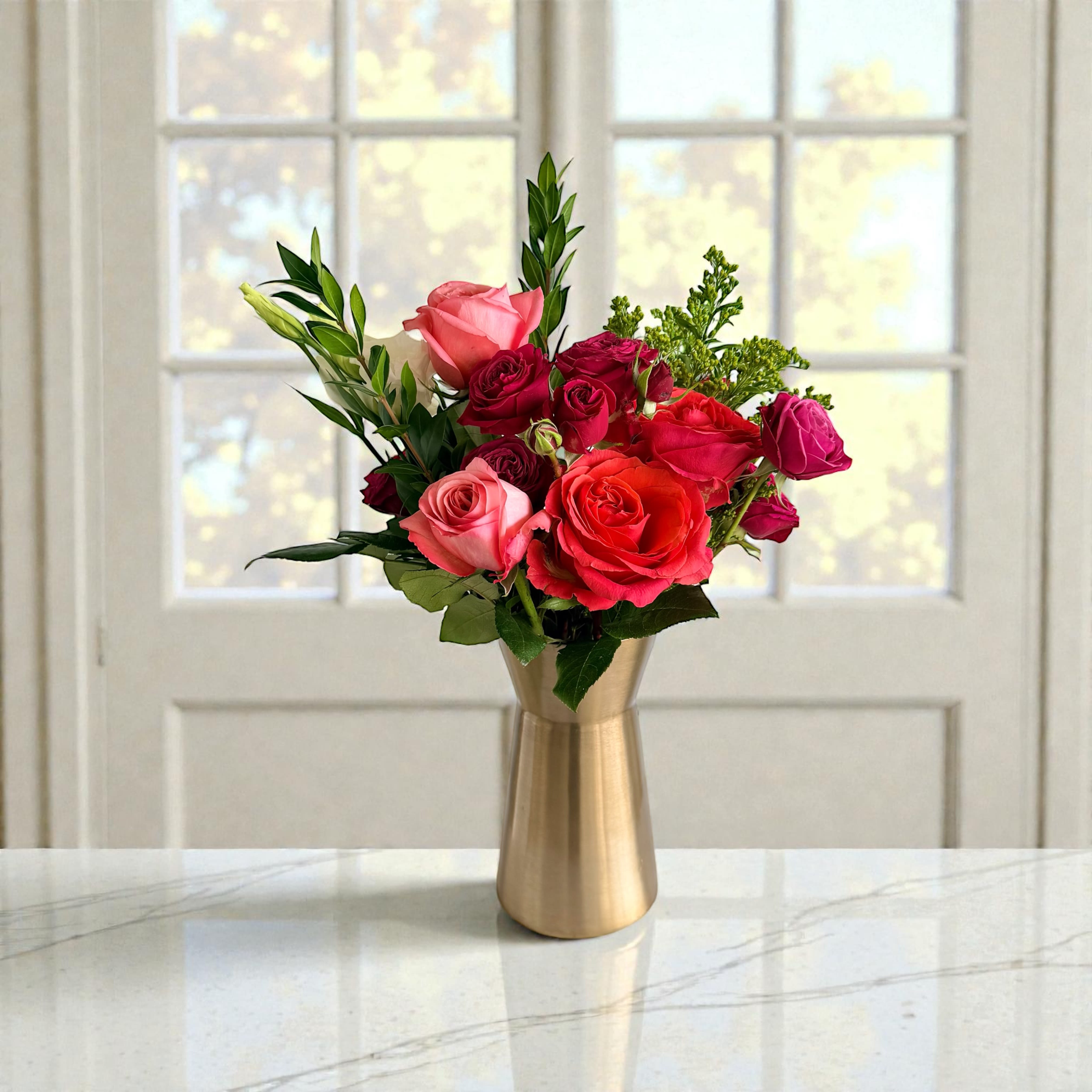Heart of Gold - Classic roses and complimentary flowers in shades of red and pink artfully arranged in a golden vase to symbolize love that shines from the heart. Colors and flowers may vary. 