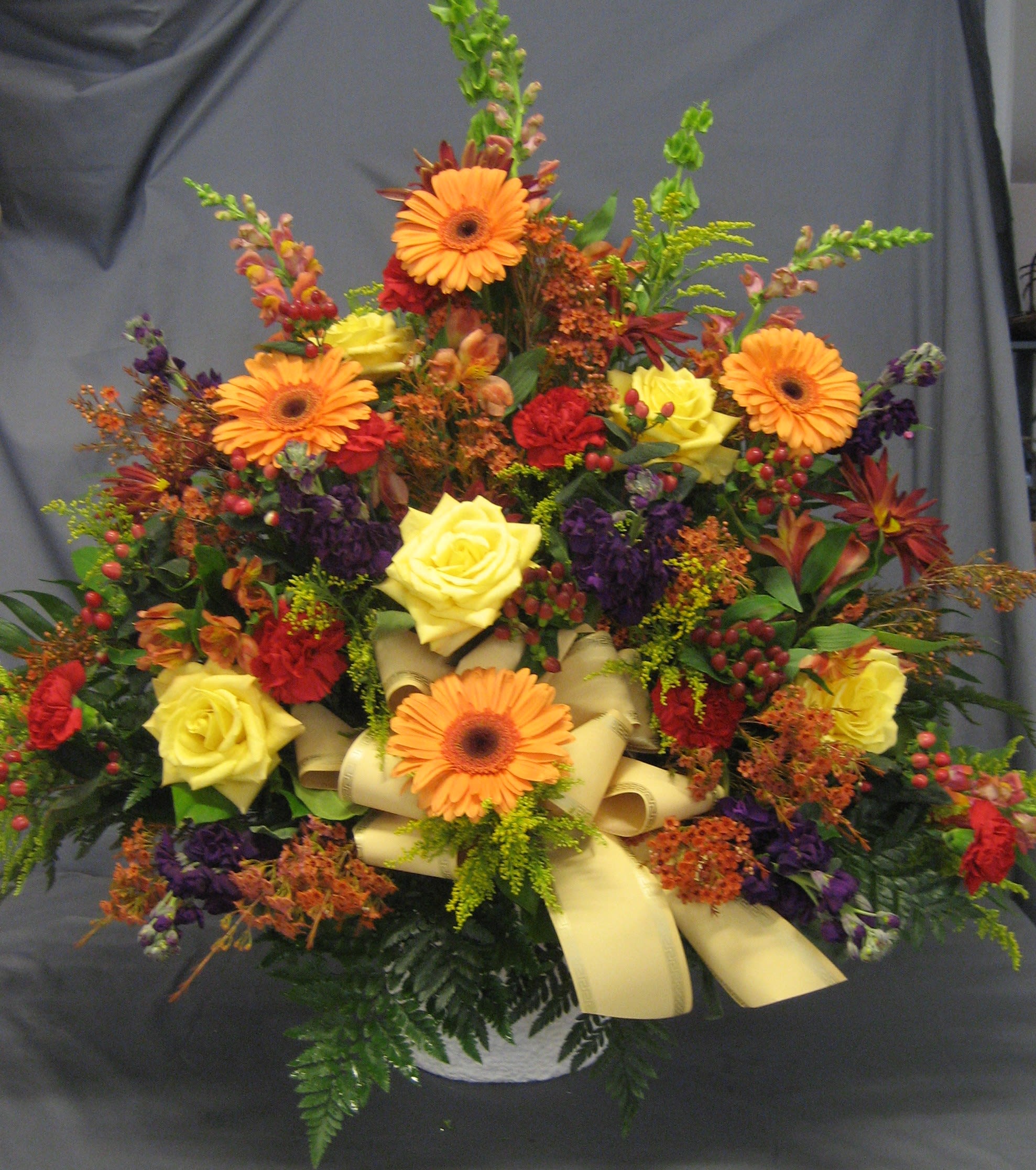 Fall Toned Mache M16 - These colors work perfect for a service in autumn or as a colorful tribute to anyone. The rich orange gerbers, sunny yellow roses and vibrant purple stock are accented with other flowers to complete the arrangement.