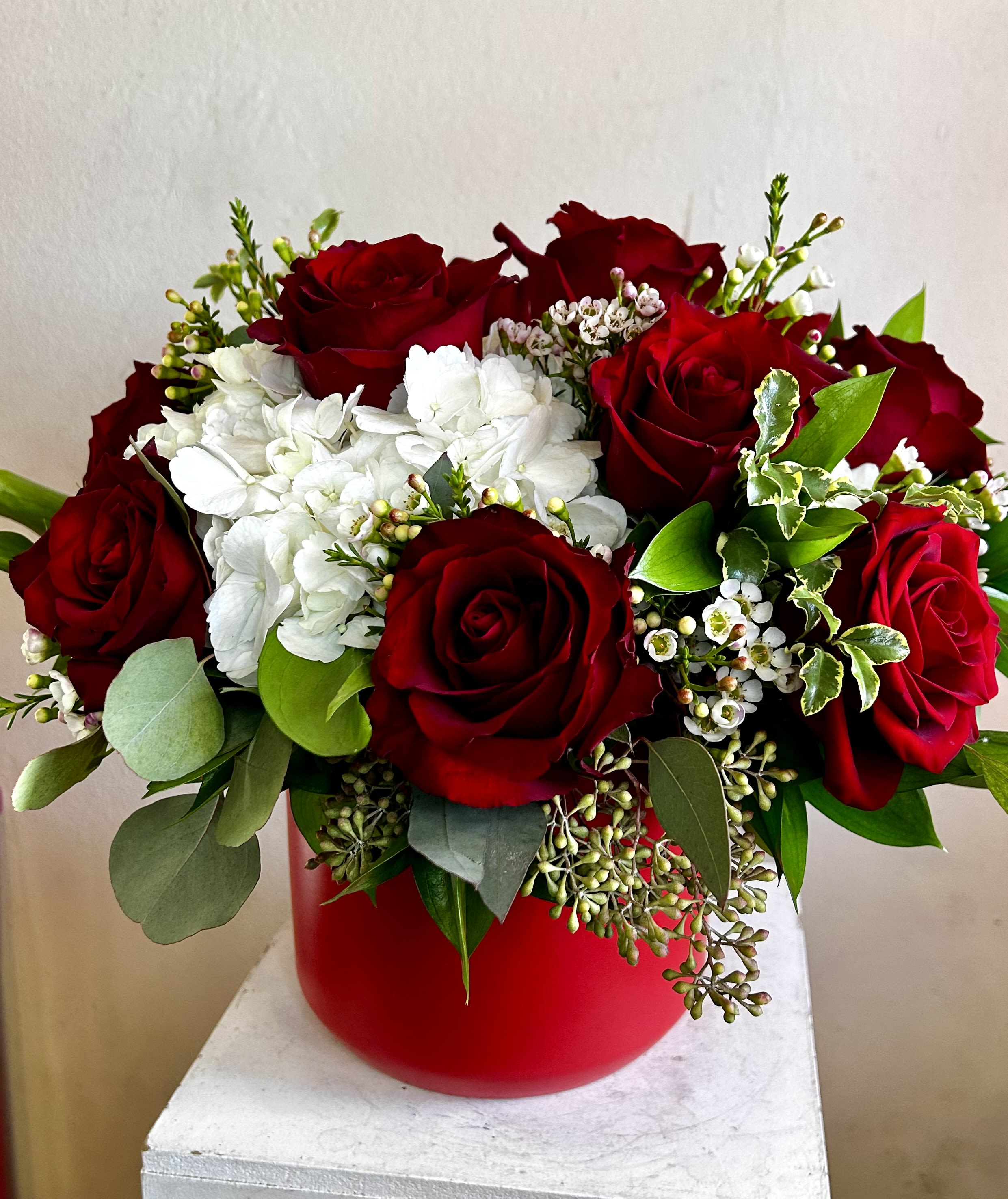 Lady in Red - Red ceramic vase filled with a dozen roses, white hydrangea and accompanying flowers.