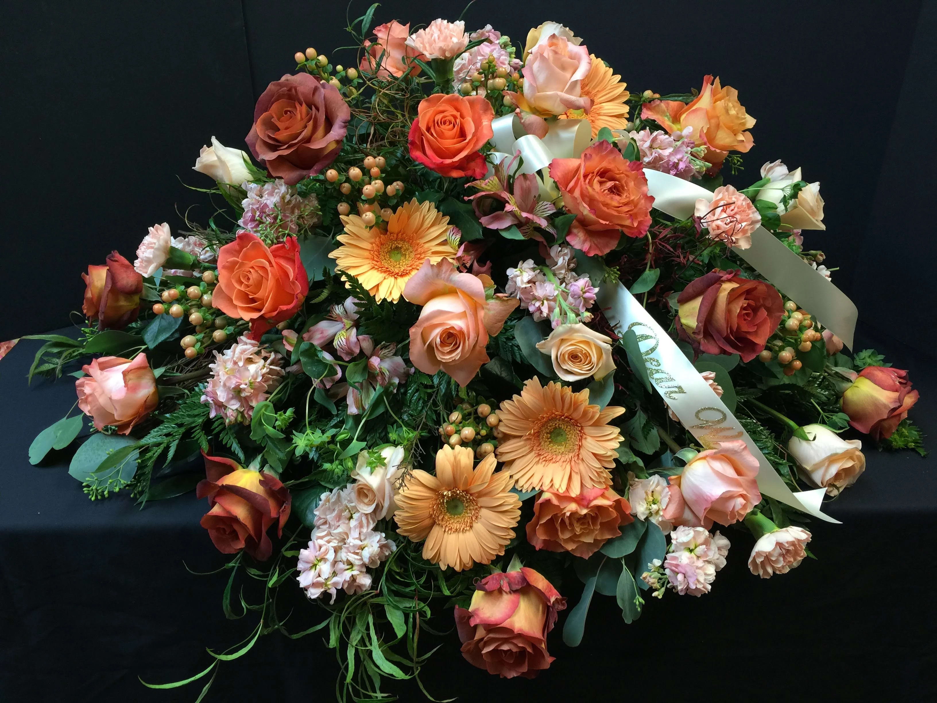 Love Blooms Casket Spray - Show your love with a mix pink, peach and orange blooms that are as gentle and pure as a cloud. Accented with a mix of greenery, fragrant flowers create a lovely and traditional casket spray. Pairs beautifully with our Open Heart Standing Spray