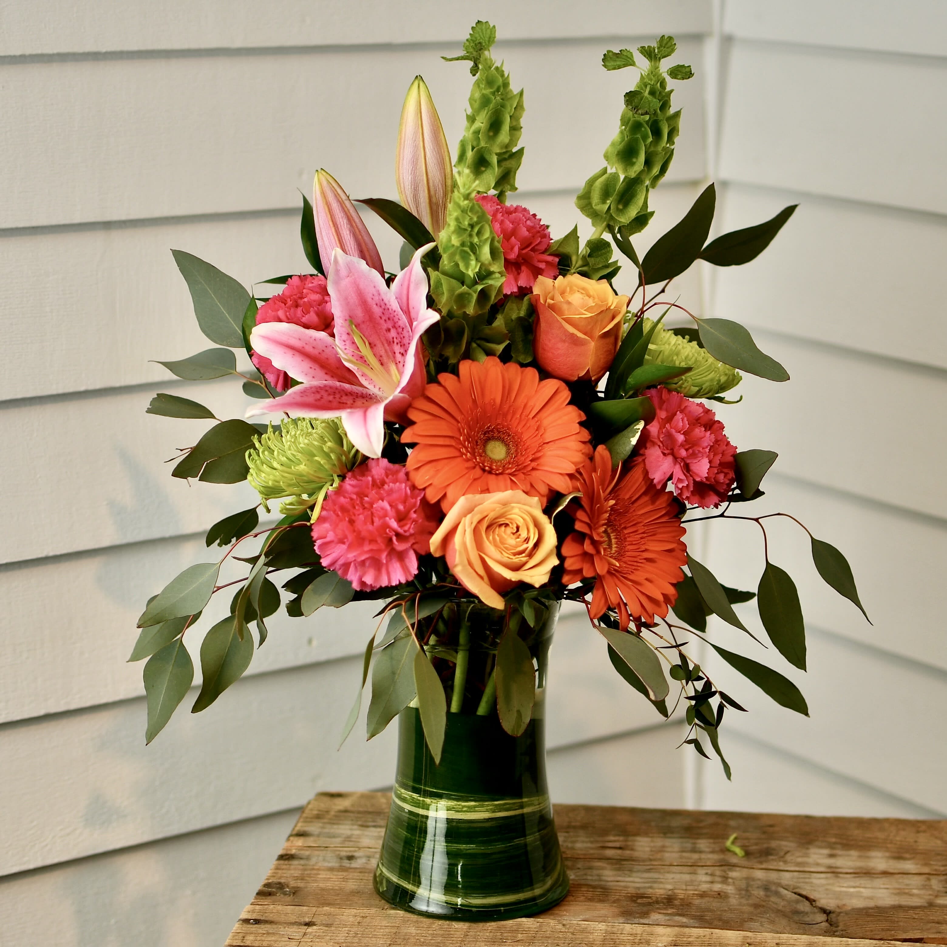 Tangerine Sunset - LOCAL DELIVERY ONY!!! Bright, uplifting, colorful arrangement of fresh flowers that includes; lilies, roses, carnations, mums, gerbera daisy's, bells of Ireland and a mix of greenery throughout. Designed in a clear glass vase. Flowers &amp; Colors may vary! ONLY AVAILABLE FOR LOCAL DELIVERY!!!