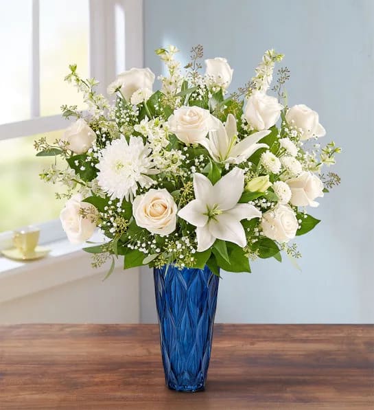 Royal Harmony - A beautiful tribute to someone so loved. Our abundant arrangement is filled with a soothing gathering of white blooms and lush greenery. Designed in a tall cobalt blue vase, it’s a touching way to honor their memory, while conveying your heartfelt condolences.  All-around arrangement with white roses, Asiatic lilies, larkspur, mums and button poms; accented with baby’s breath, eucalyptus and assorted greenery Artistically designed in a tall cobalt blue vase  Large arrangement measures approximately 30"H x 18"W Small arrangement measures approximately 29"H x 16"W Appropriate for sending to the homes of family members or friends Our florists hand-design each arrangement, so colors and varieties may vary due to local availability To ensure lasting beauty, lilies may arrive in bud form and will fully bloom over the next few days Vase is subject to availability.