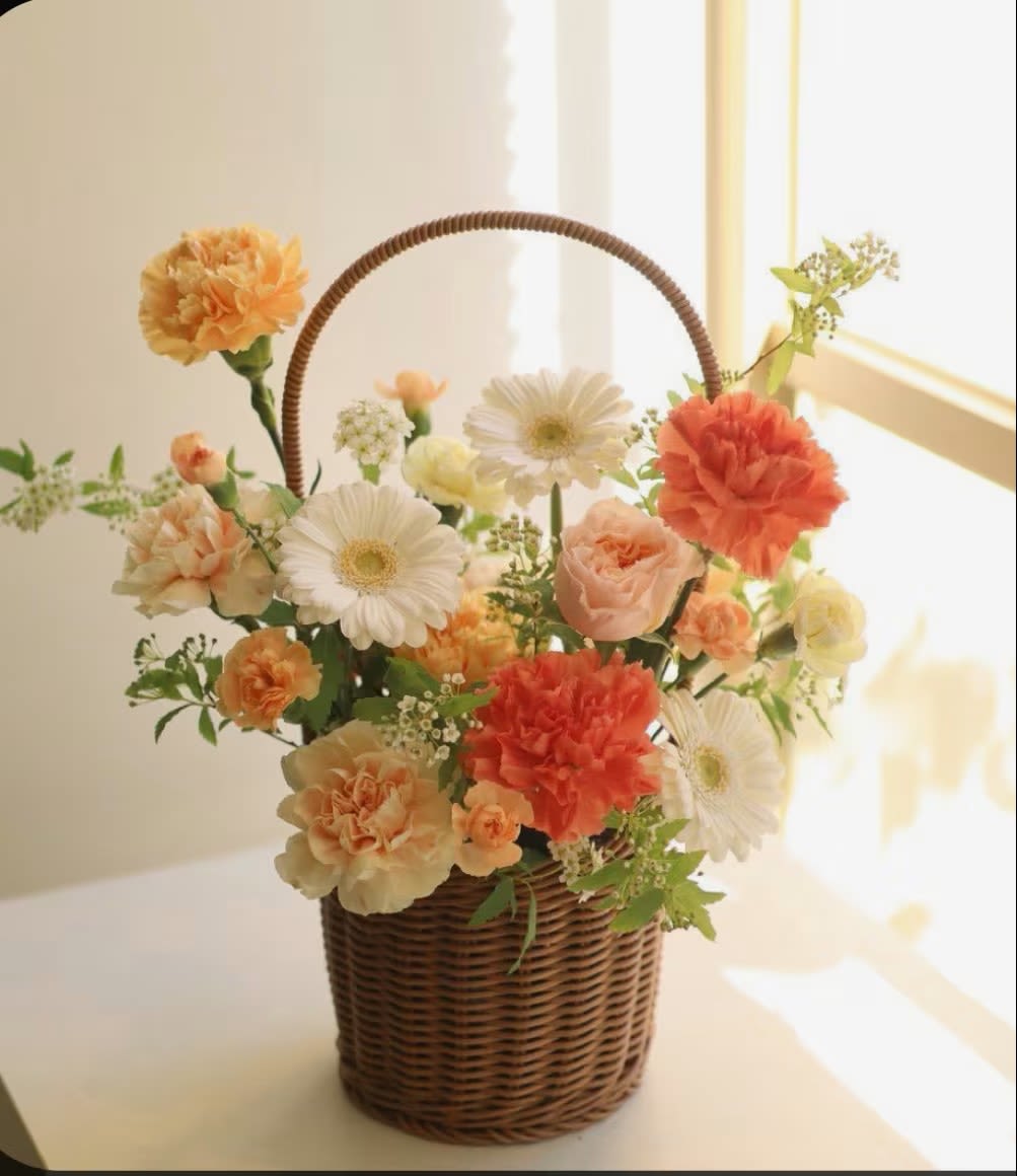 Apricot Morning - Bring the glow of sunshine indoors with Golden Hour Blooms. Featuring peach carnations, creamy roses, cheerful gerberas, and pops of orange nestled in a charming woven basket, this arrangement radiates warmth and happiness. A perfect gift for brightening someone’s day, celebrating milestones, or simply adding a touch of joy to your home.