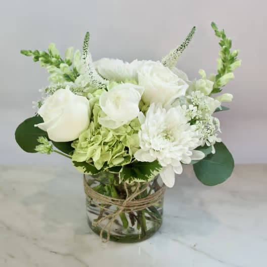 Whispers of White - A timeless display of pure elegance, this hand-crafted arrangement features lush white roses, hydrangea, snapdragons, with tiny accents and fresh greenery. Styled in a clear glass vase wrapped with rustic twine, it’s perfect for weddings, sympathy, or simply bringing a touch of serene beauty into any space.