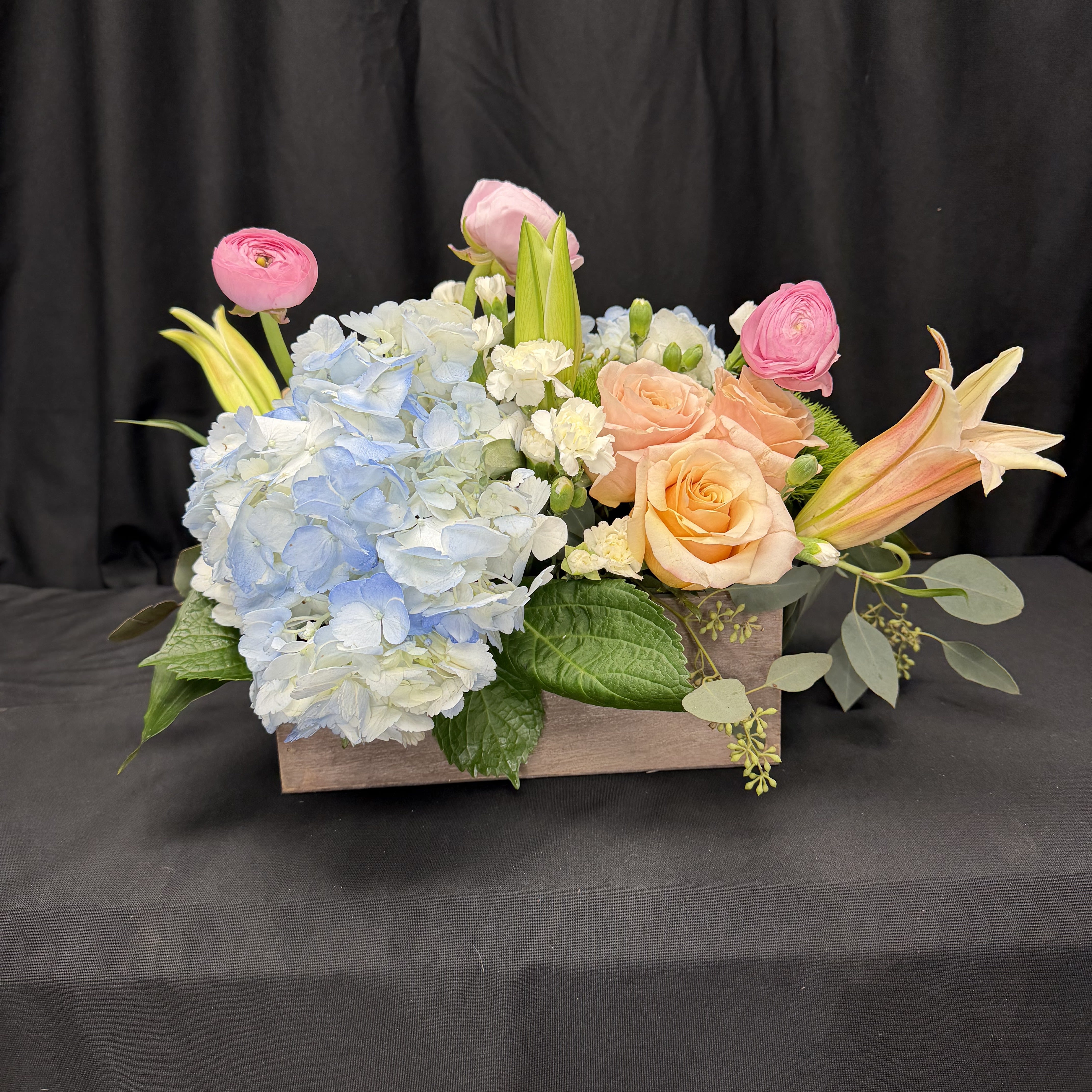 Forever Yours - Soft, romantic, and timeless, Forever Yours is a Valentine’s Day arrangement designed to express love with elegance rather than extravagance. Featuring a delicate blend of blush roses, airy blue hydrangea, charming ranunculus, and seasonal accents, this arrangement is artfully styled in a natural wooden box for a warm, modern finish.  Perfect for Valentine’s Day, anniversaries, or simply reminding someone how much they mean to you, Forever Yours speaks in gentle tones of affection and grace—because some sentiments never go out of style.