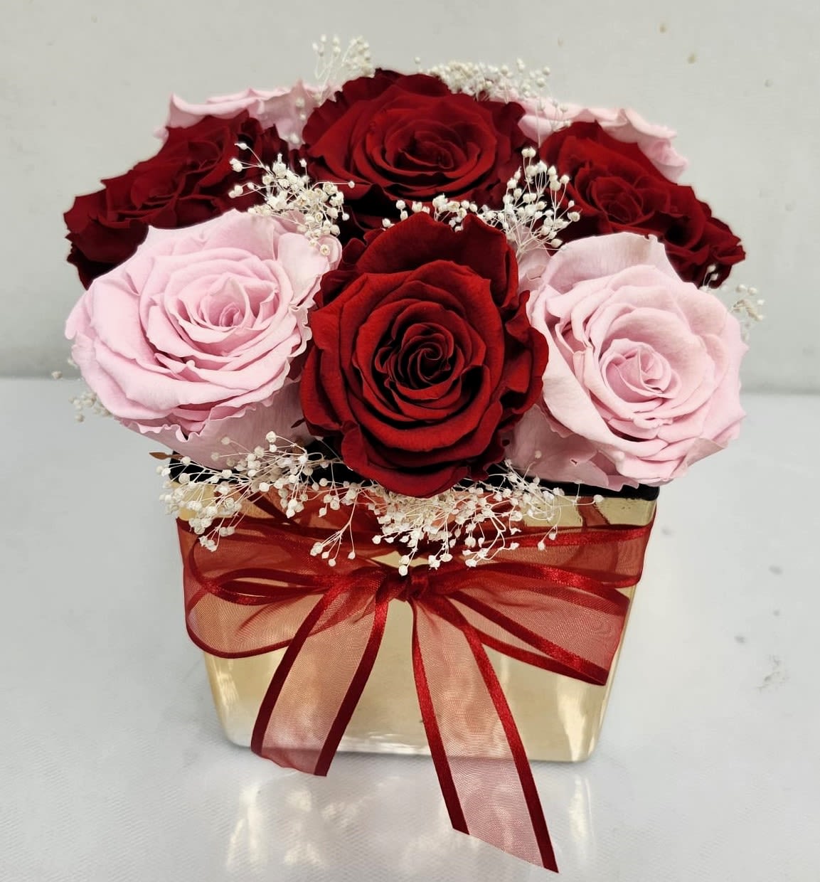 Amor Mio (PRESERVED ROSES) - 9 Beautiful "Preserved" Roses in shades of pink and red, with a touch of Baby's Breath, in a square gold ceramic vase. Preserved Roses will last over a year.