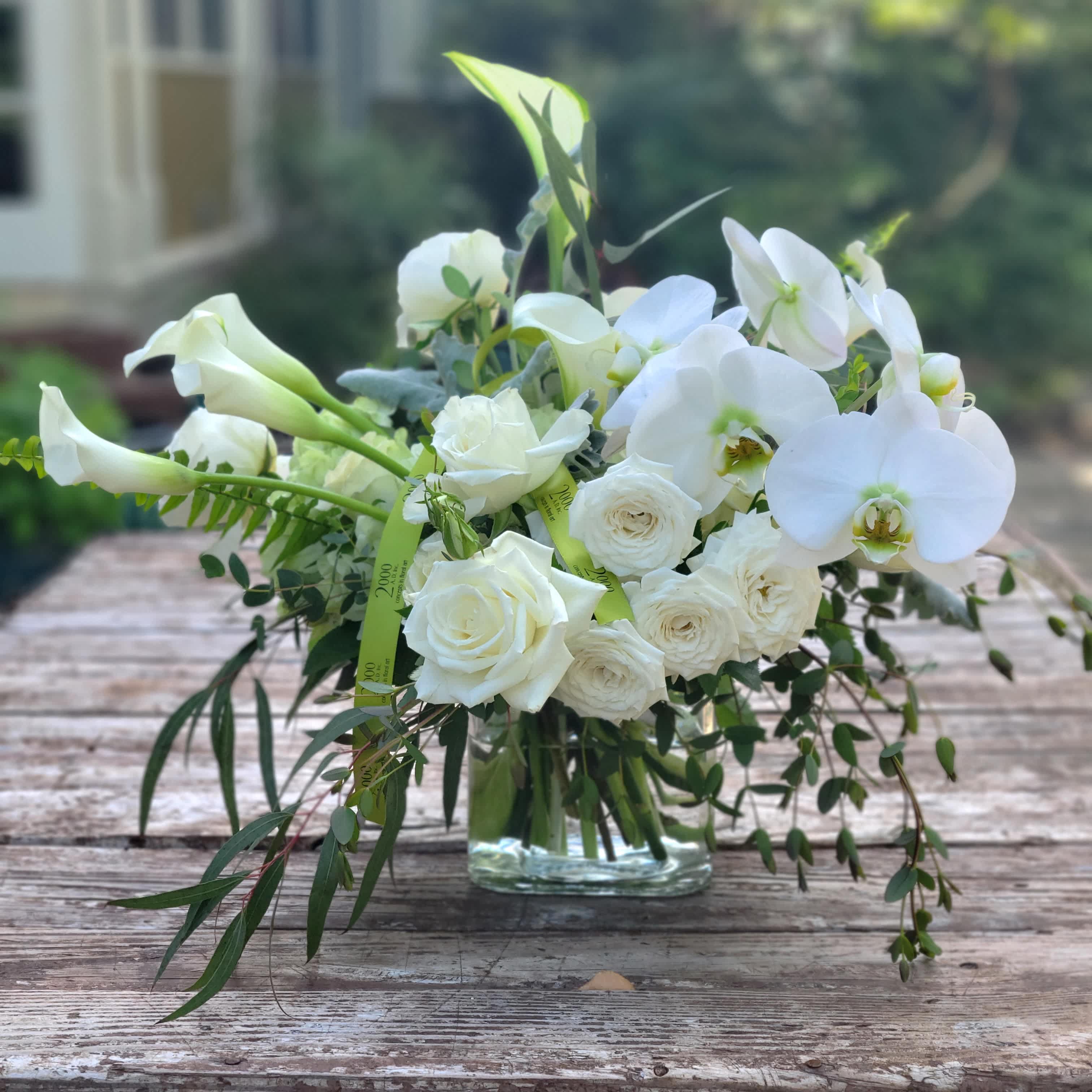 Blanca - Joyful composition of white blooms in a variety of sizes and textures that brings joy and the knowing of a better tomorrow. Accented with various seasonal foliages. Presented in a clear glass container with exposed stems.