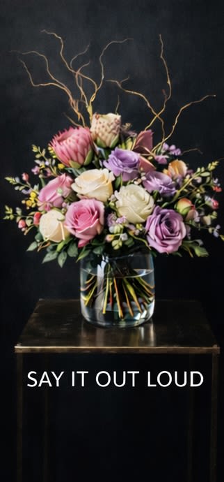 Say It Loud - Arrangement - Timeless, romantic, and effortlessly refined. This arrangement is led by premium garden roses selected for their full, ruffled petals and exceptional depth of color, anchored by luminous Queen’s Crown and Playa Blanca. A sculptural protea adds a modern focal point and textural contrast, while delicate waxflower keeps the composition bloom-forward and airy. Finished with graceful, architectural branches for height and movement, this piece feels classic, polished, and deeply heartfelt.  PART OF OUR LOVE IN EVERY ERA — ARRANGEMENT COLLECTION Featuring Say It Out Loud, The Story We Tell, and Midnight Moment  This Valentine’s collection is intentionally bloom-forward, designed around a tightly curated selection of premium garden rose varieties chosen for their exceptional petal quality, fragrance, and presence. To honor the integrity of each design, we are limiting our Valentine’s stock to these featured blooms, allowing the roses — and their natural beauty — to take center stage. Our arrangements are lush, expressive, and refined, accented with delicate waxflower, sculptural protea, and elegant branching to create movement, depth, and lasting visual impact.  Images shown are renderings and are representative of overall size, style, and color palette.