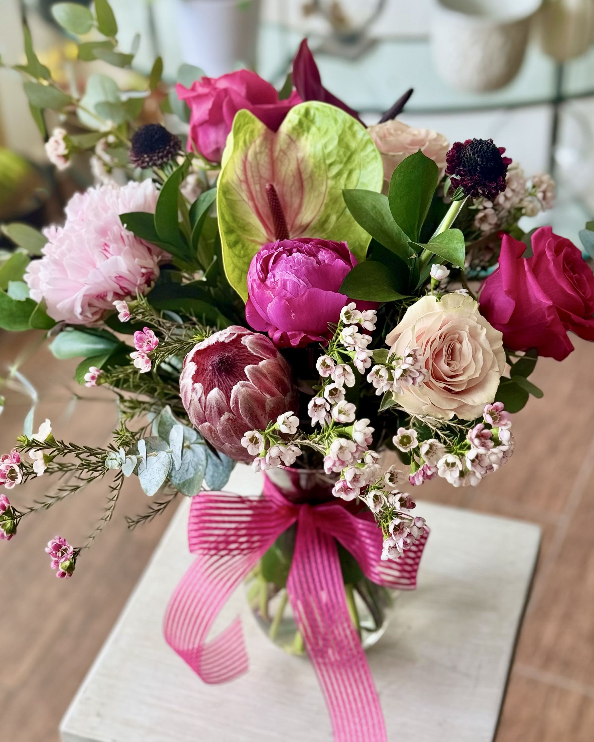 Penelope - Big blooms that impress. Protea, peonies, roses, anthurium arranged in a clear glass vase. 