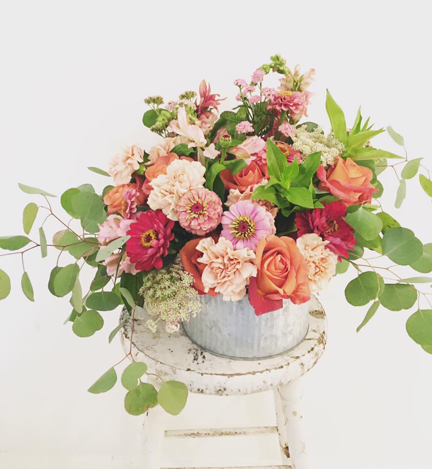 The Ashlynn - (The above arrangement is pictured as a DELUXE)  Although zinnias begin their bloom in summertime, we'll substitute these with some other beautiful flowers that showcase the sunny freshness of a warm spring day. I love that this arrangement has a country feel that's both down to earth and happy, and is loaded with color and eucalyptus.  *** Please NOTE: Do to the Covid-19 shutdowns, flower substitutions will most likely occur but we will strive to make them even more gorgeous than the photos :)