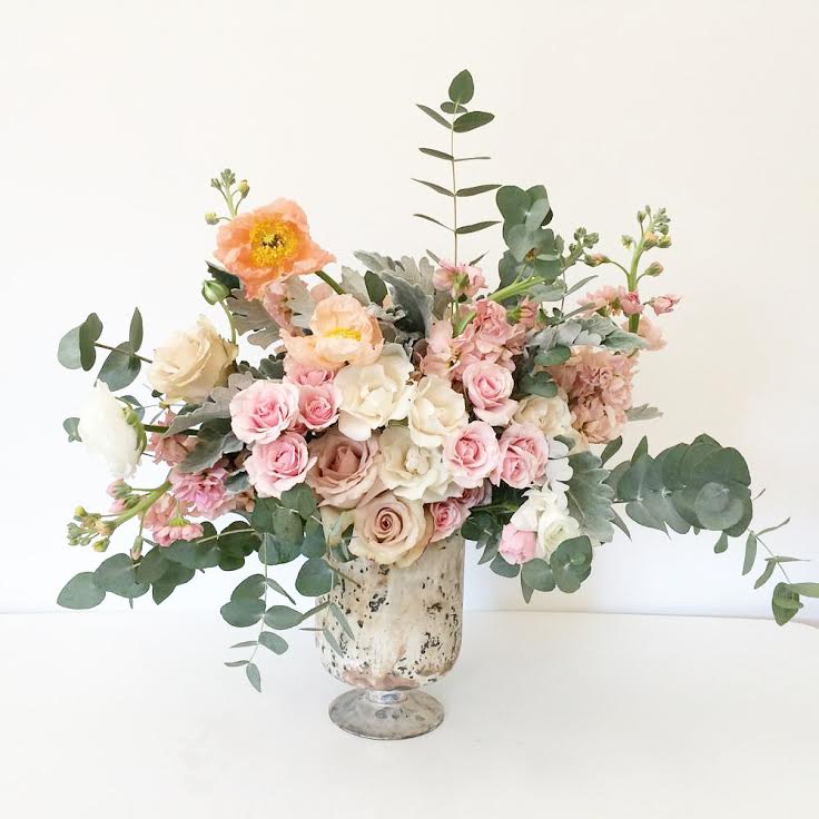 The Penelope - A sweet collection of soft pastel flowers and lush greenery. Each arrangement is thoughtfully designed and may include a mix of spray roses, garden roses, ranunculus, wildflowers, and other seasonal blooms, beautifully presented in a mercury glass vase.  Please note: The DELUXE version is the one pictured. 