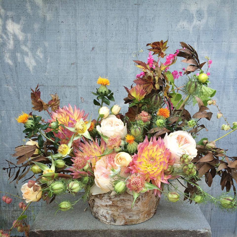 Sunset in the Forest - This arrangement highlights a striking focal bloom — garden roses, jumbo dahlias, or proteas — complemented by airy details and touches of fall foliage. Designed in a variety of unique woodland basins, this piece is the definition of fall beauty.