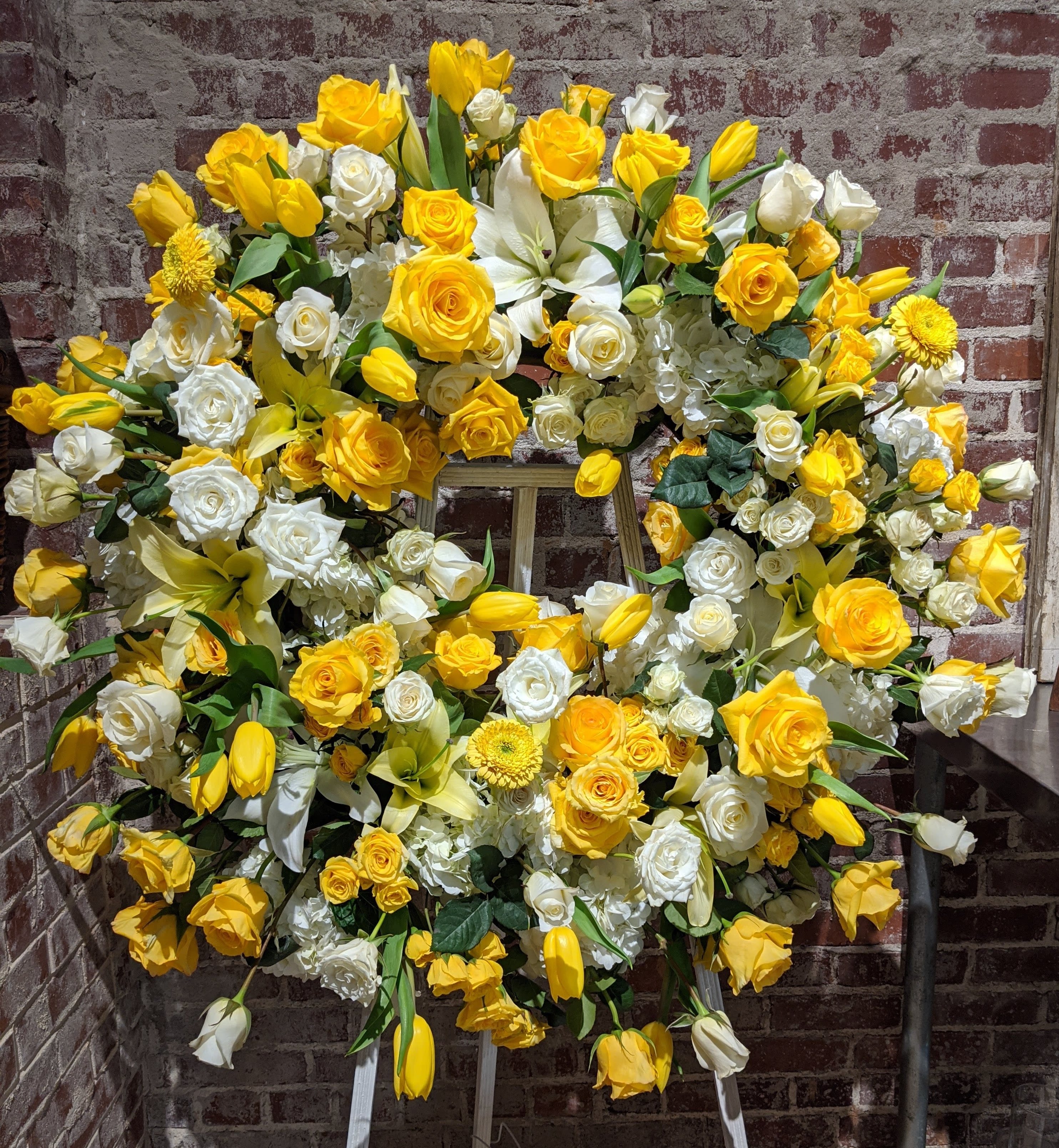 Warmest Thoughts Memorial Wreath - A beautiful floral tribute for the deceased. A lush palette of white and yellow blossoms accented with soft green foliages create a sophisticated statement for this celebration of life. Additional color palettes are available upon request. 48 hours notice is required for a color substitution. Please call the shop at 404-314-6194 to discuss.
