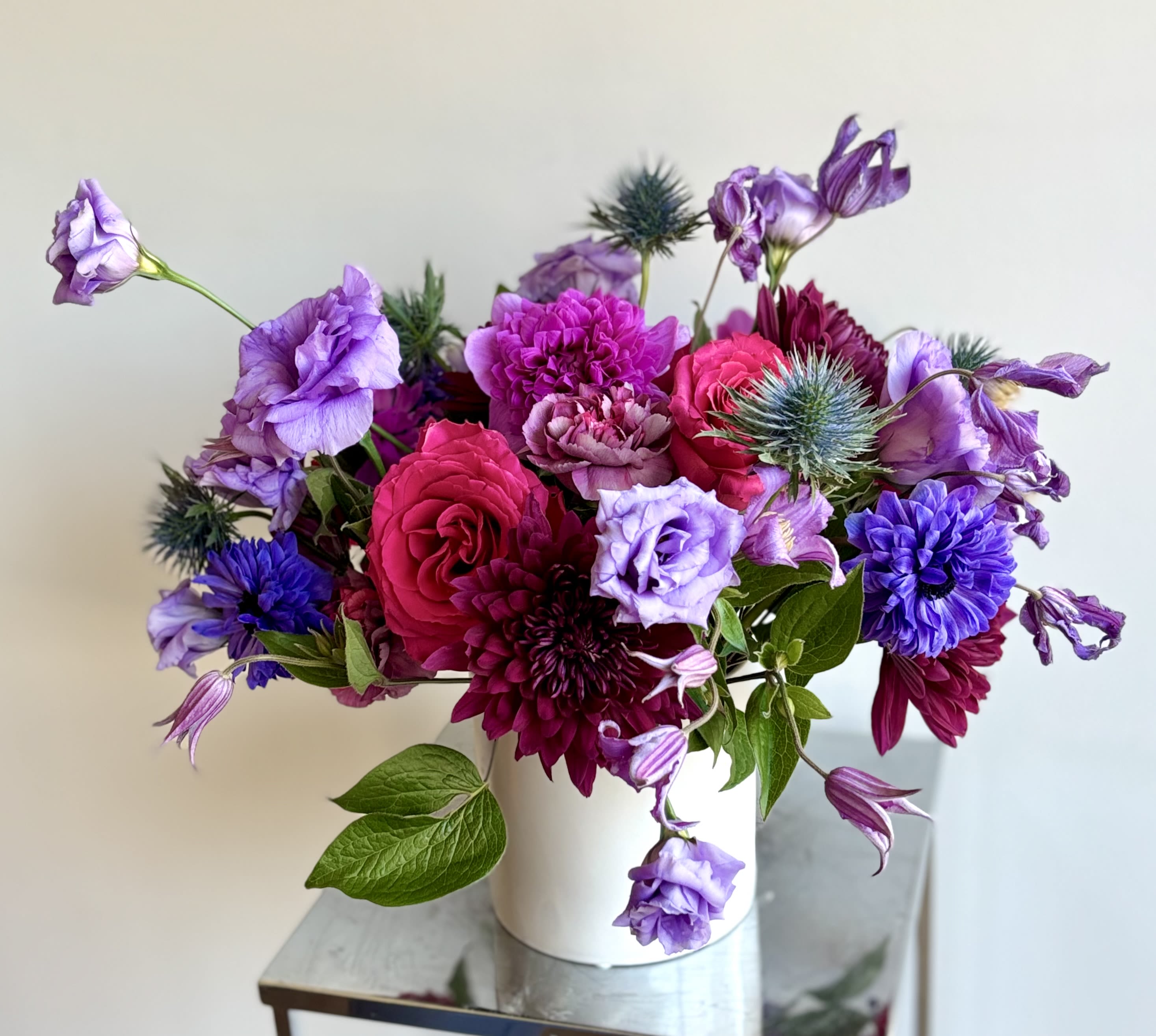 Berry Electric - For your Jewel. A gorgeous flower arrangement of premium flowers in berry tones designed in a 5inch white ceramic vase. The mix of flowers usually has roses, cremons, full star anemones, hyacinths, clematis and lisianthus and greenery. The selection may vary based on the availability.