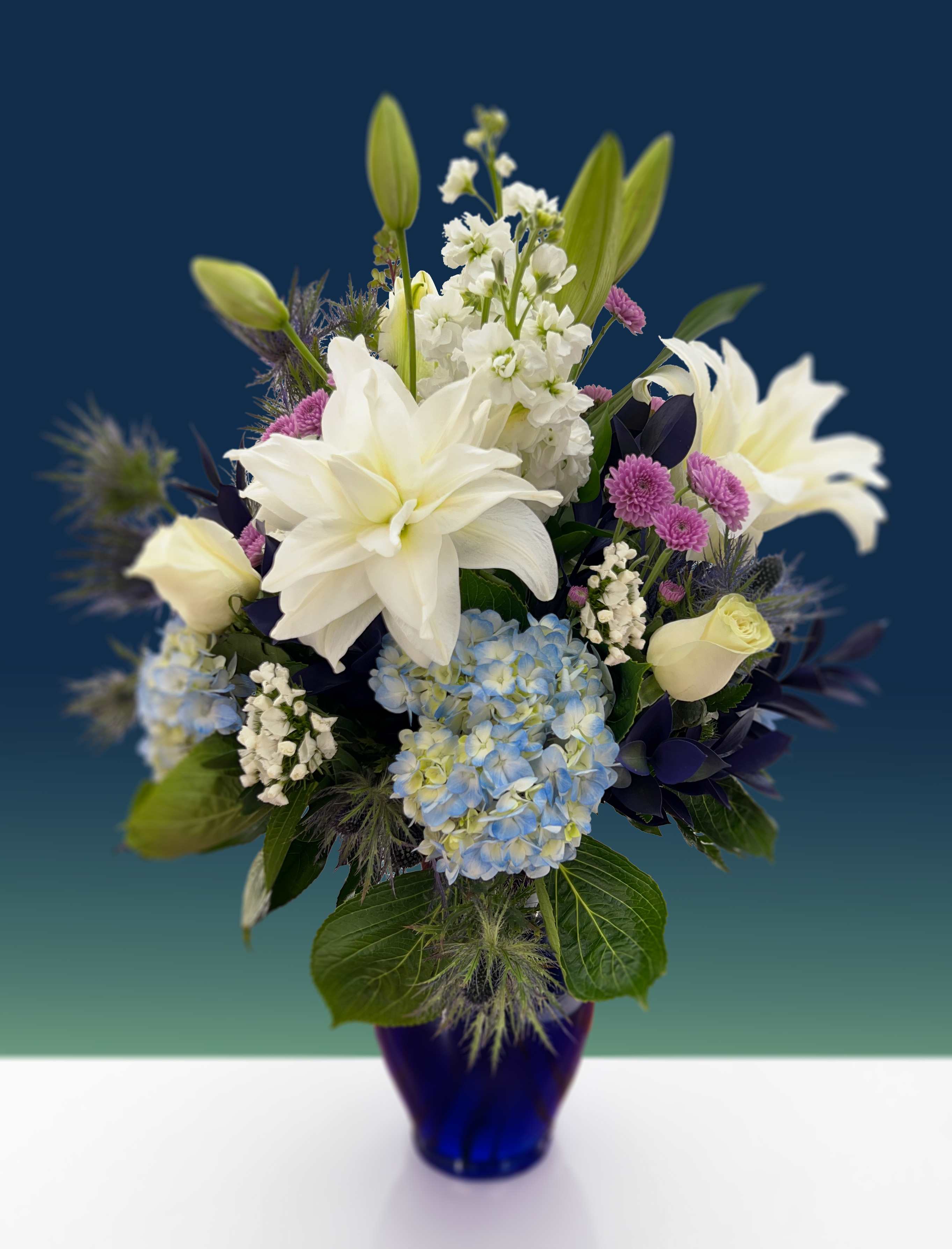 Blue Sky - This arrangement is composed of blue thistle, blue hydrangeas, white lilies, white roses, and dark blue ruscus.