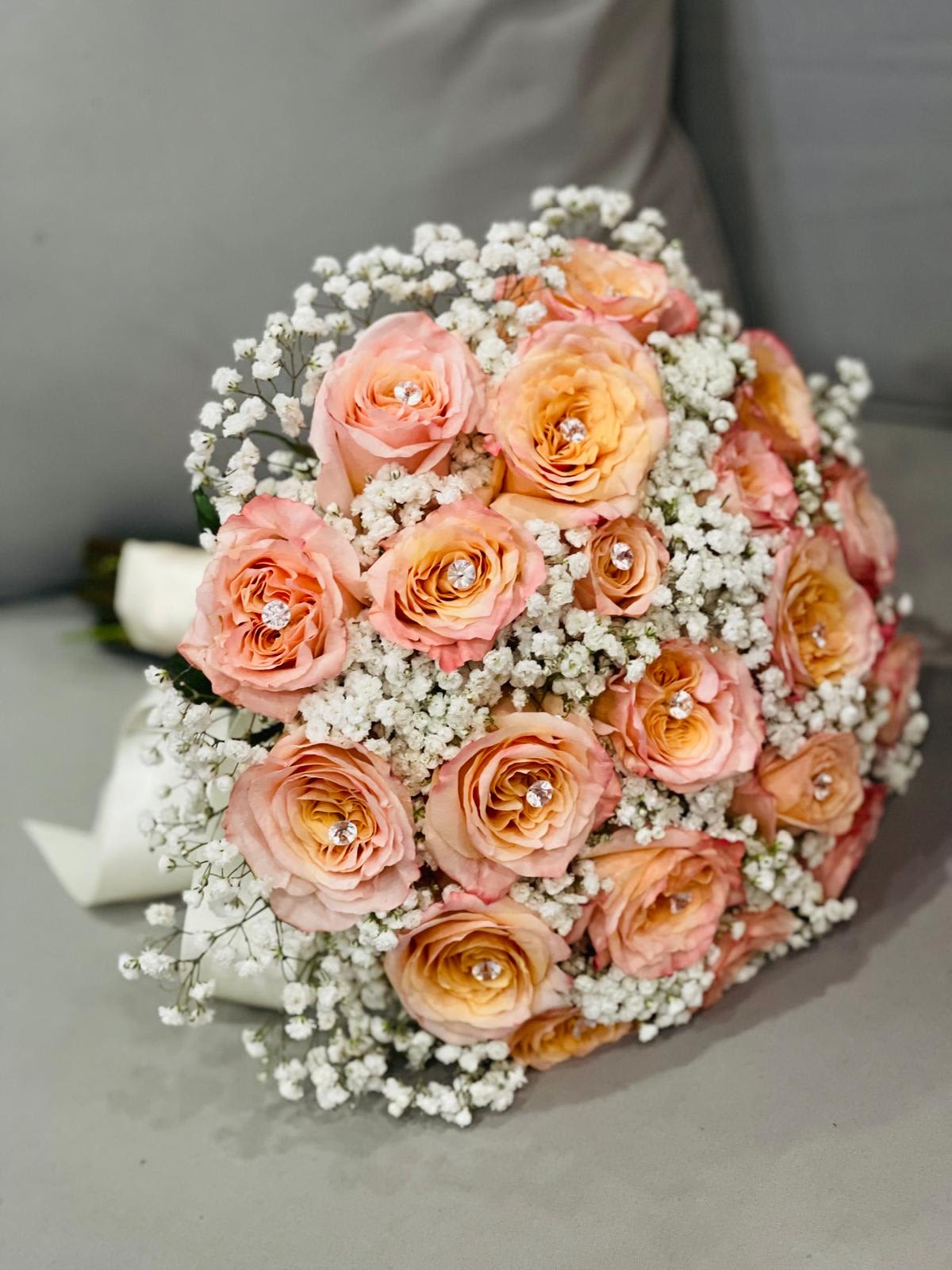 Rose Whispers - Rose Whispers* is a delicate bridal bouquet crafted with timeless elegance. It features:    - **Roses:** A blend of pristine white roses and soft blush roses, symbolizing purity, love, and romance.   - **Baby’s Breath:** Ethereal clusters of tiny white blooms create a cloud-like effect, adding softness and grace to the arrangement.    The bouquet is tied with a flowing silk ribbon in ivory or soft pink, completing its classic and romantic aesthetic. Perfect for a bride seeking simplicity and charm on her special day.  