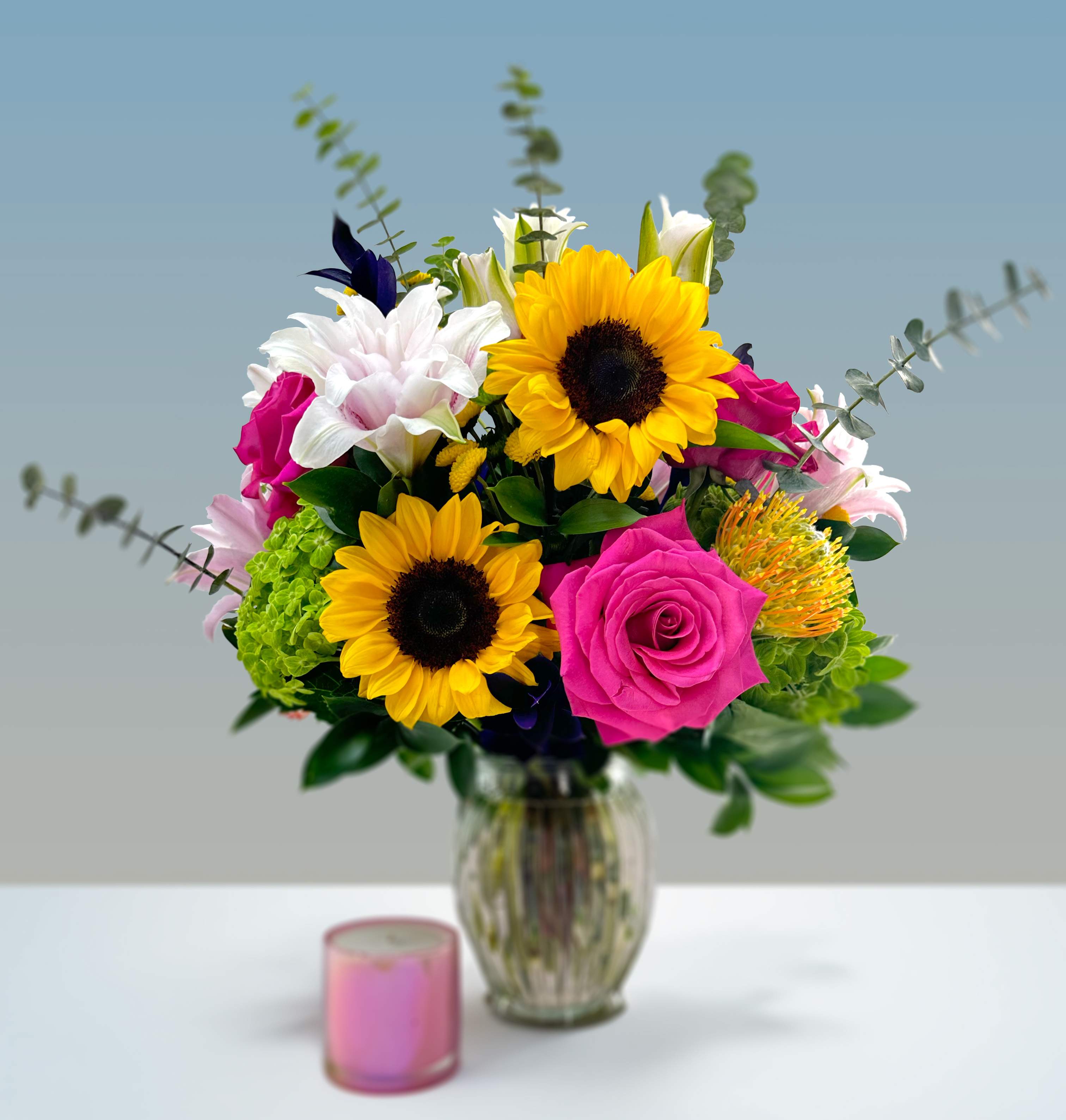 Isabella - Regality and innocence come to mind with this bouquet of hydrangeas, pink floyd roses, sunflowers, pink lilies, pincusion protea, buttons, and other seasonal blooms.