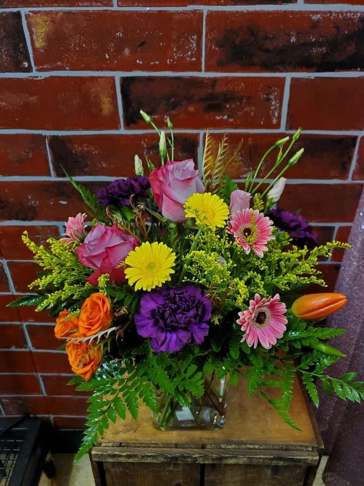 Color Me Colorful - This bouquet is designed one sided in a rectangle vase. Flowers include Purple roses, Yellow and Pink Micro Gerbs, Spray rose, Tulip, Deep Purple Carnation with yellow solidago as filler flower.  *Some stages of flower life may vary. (Example: Lilies may be more open than imaged.)  Flower shortages and product availability means that some substitutions will apply. Value will always be filled.  This bouquet might include eucalyptus amongst the greenery. It may be toxic to pets including but not limited to Cats and Dogs if digested.