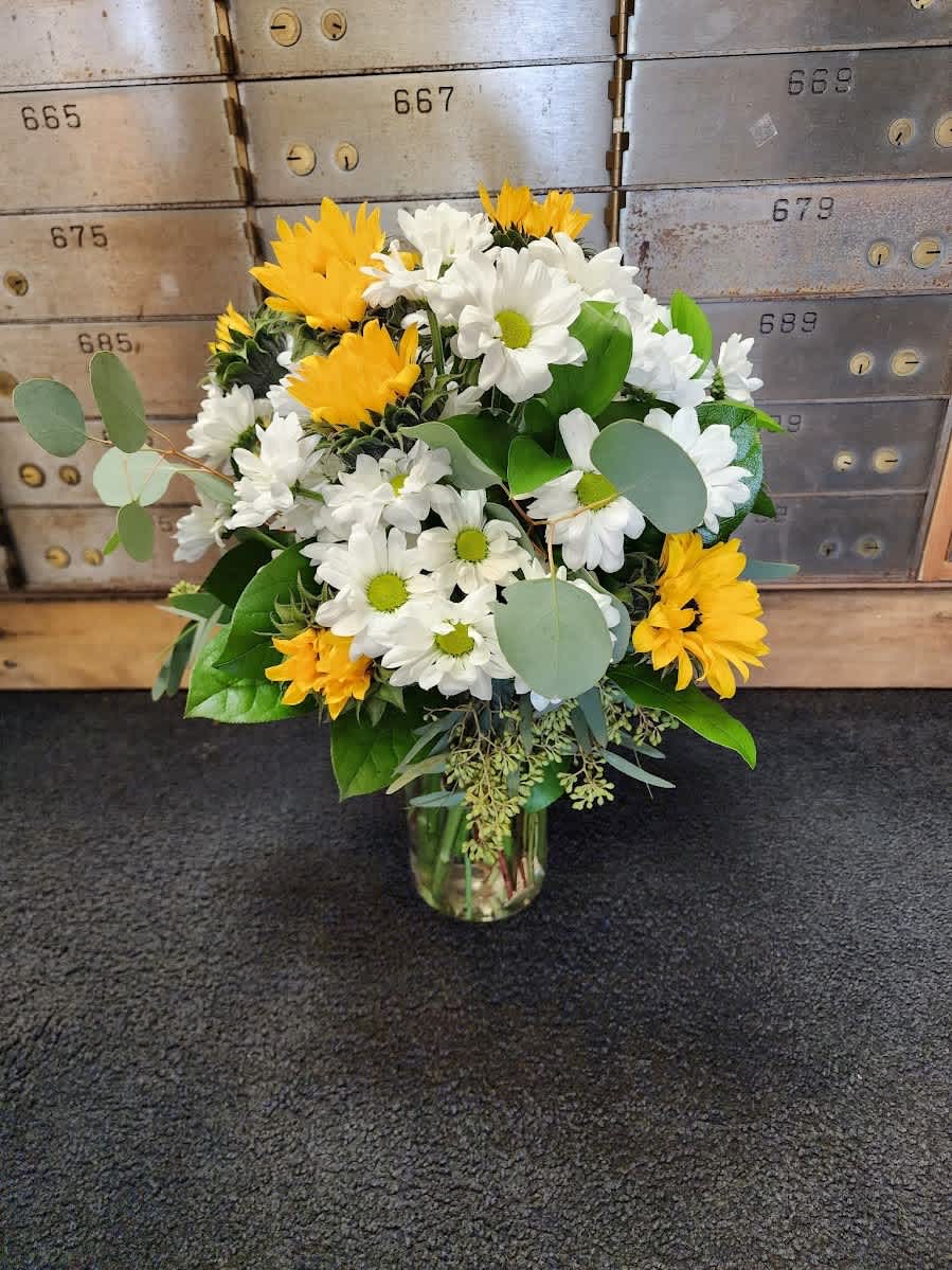 Sunflowers and Daisies - An all around flower arrangement designed with fresh flowers to include sunflowers, daisy poms and gerbera daisies in white and yellow.  * Some stages of flower life may vary. (Example: Lilies may be more open than imaged.)   Flower shortages and product availability means that some substitutions will apply. Value will always be filled.  This bouquet might include eucalyptus amongst the greenery. It may be toxic to pets including but not limited to Cats and Dogs if digested.