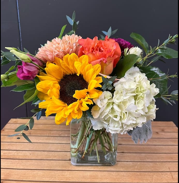 Sunny Little Sunflower - This bouquet is designed one sided with a sunflower, rose, cremone, lisianthus, carnations and Hydrangea.  *Some stages of flower life may vary. (Example: Lilies may be more open than imaged.)  Flower shortages and product availability means that some substitutions will apply. Value will always be filled. This bouquet might include eucalyptus amongst the greenery. It may be toxic to pets including but not limited to Cats and Dogs if digested.