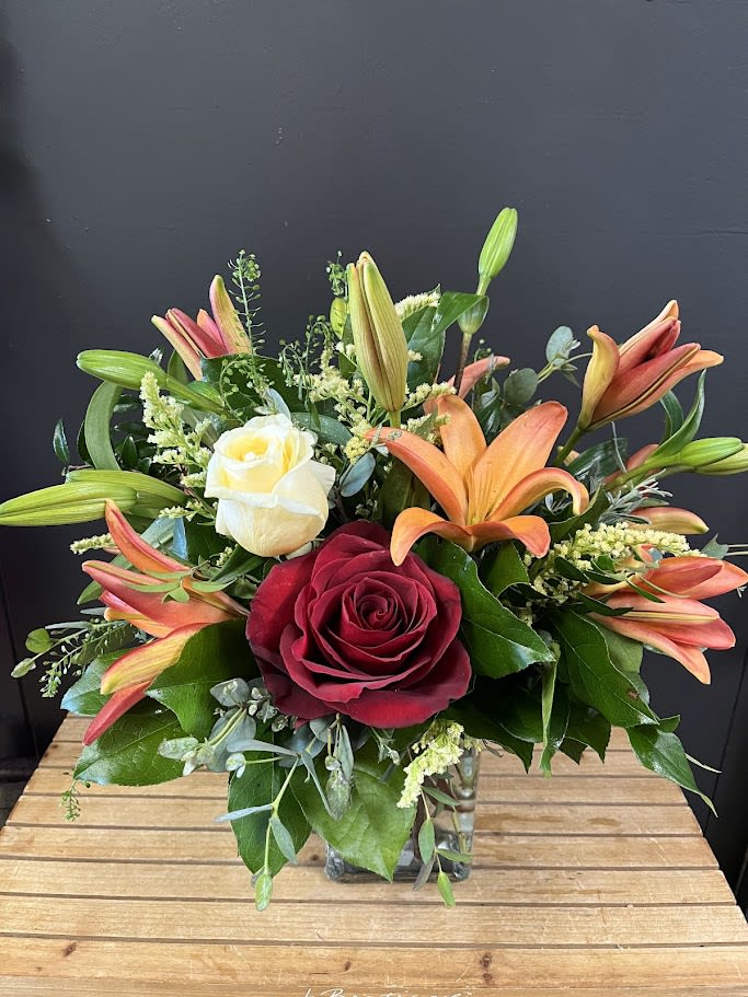 My Love, My Friend - This front sided flower arrangement designed with fresh flowers to include 1 red rose and 1 yellow rose to signify friendship and love surrounded by orange lilies and lots of beautiful greens.  * Some stages of flower life may vary. (Example: Lilies may be more open than imaged.) Flower shortages and product availability means that some substitutions will apply. Value will always be filled. This bouquet might include eucalyptus amongst the greenery. It may be toxic to pets including but not limited to Cats and Dogs if digested.