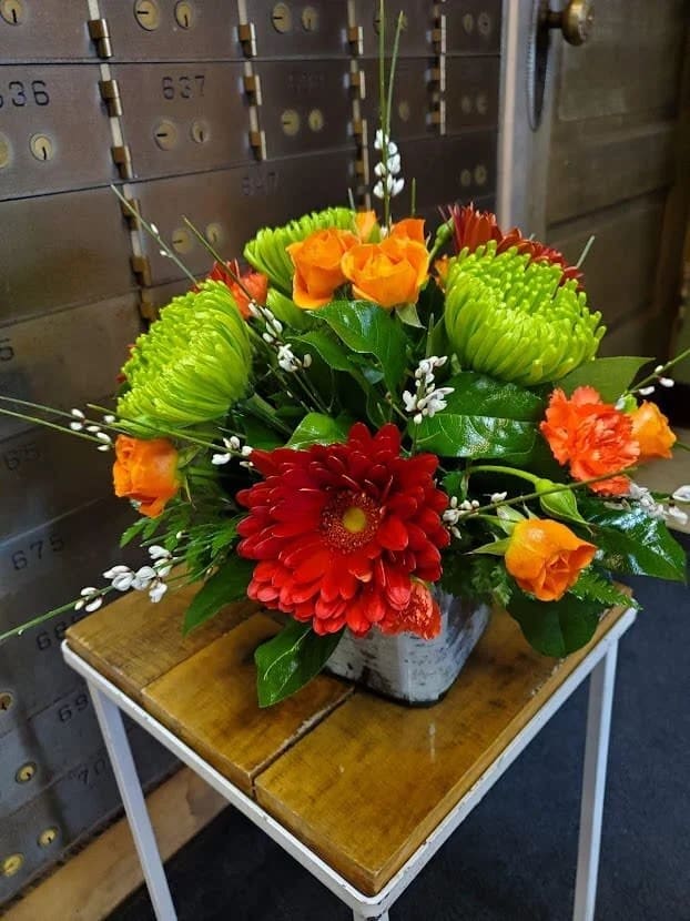 Orange, Green &amp; Red in a Square - Designed with fresh flowers to include orange spray roses, green spider mums and red gerbera daisies. This is an all around bouquet in a cube vase.  * Some stages of flower life may vary. (Example: Lilies may be more open than imaged.)  Flower shortages and product availability means that some substitutions will apply. Value will always be filled.  This bouquet might include eucalyptus amongst the greenery. It may be toxic to pets including but not limited to Cats and Dogs if digested.