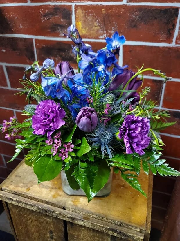 Twilight Harmony - Bring elegance and serenity to any space with our Twilight Harmony Bouquet, featuring vibrant blue delphinium, striking blue thistle, soft purple carnations, graceful purple tulips, and complementary purple filler flowers, all beautifully arranged in a modern square vase. This harmonious blend of cool tones and varied textures creates a stunning visual statement, perfect for birthdays, celebrations, or thoughtful gifting.  Hand-selected for freshness and artfully arranged to highlight each bloom, this bouquet is delivered with care by Adorkable Flowers and Gifts, offering a sophisticated gift that delights the eye and lifts the spirit.  * Some stages of flower life may vary. (Example: Lilies may be more open than imaged.)  Flower shortages and product availability means that some substitutions will apply. Value will always be filled. This bouquet might include eucalyptus amongst the greenery. It may be toxic to pets including but not limited to cats and dogs if digested.