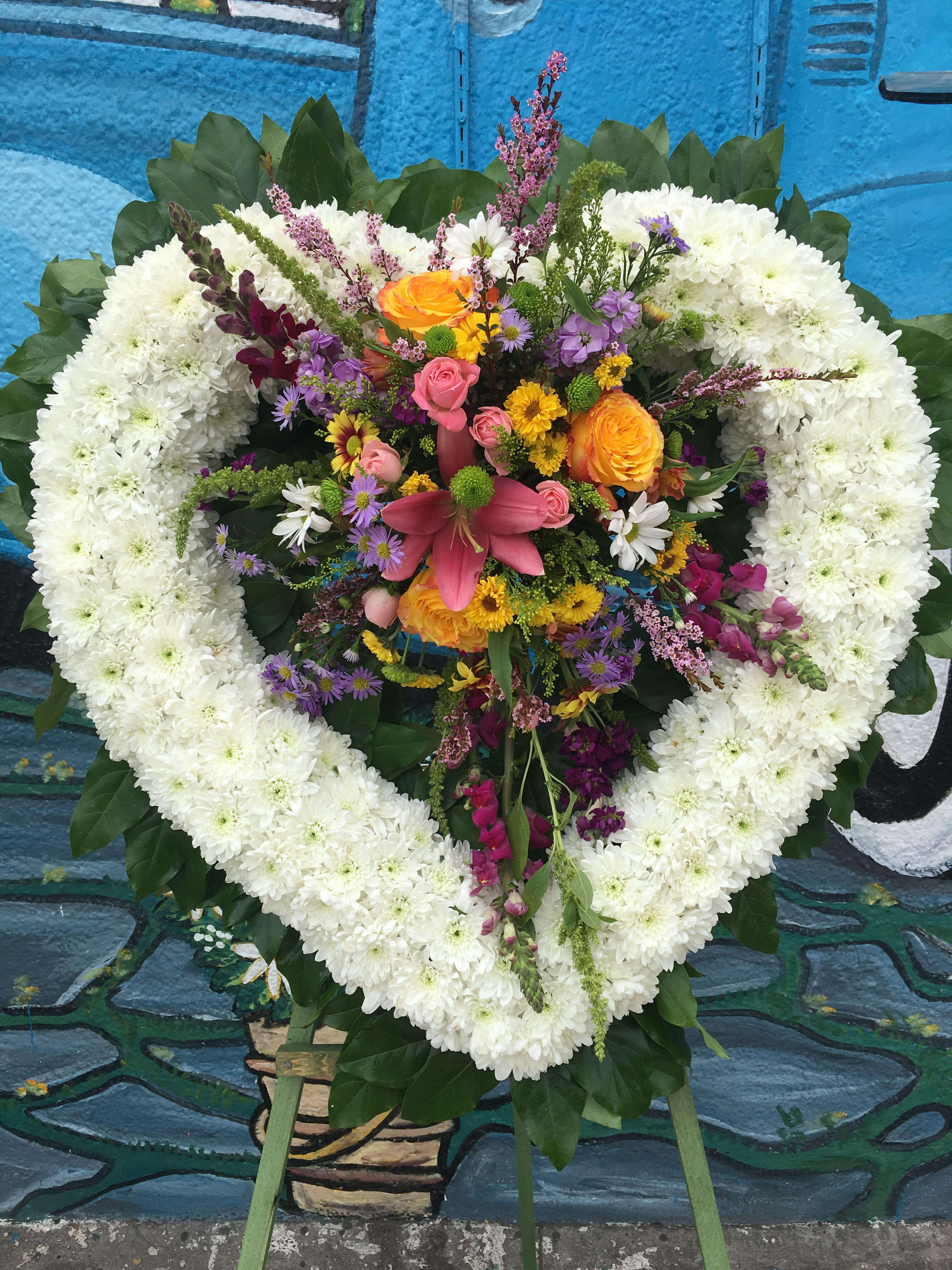 Spring in the Heart  - Heart wreath includes white daisy cushion, floral arrangement with spring flowers  includes wood stand.  *PHOTO PICTURED IS THE PREMIUM PRICE*  *Order must be placed 2 - 3 days in advance* (Please note, same day pick-up or delivery is not available for this product) 