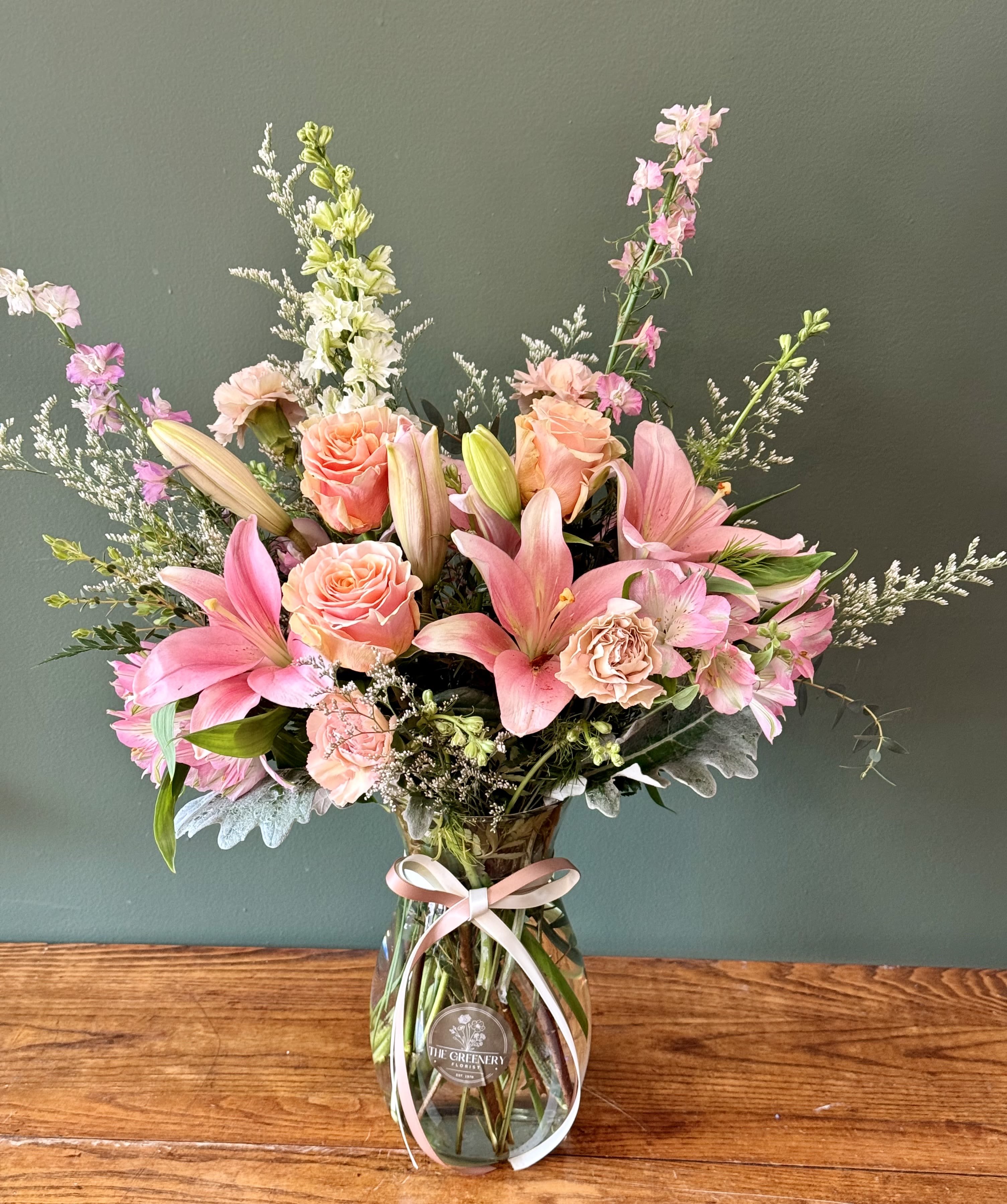 Shades of Pink - A soft, romantic floral arrangement featuring beautiful blooms in layered shades of pink. Elegant, fresh, and perfect for any occasion. Featuring: - Ecuadorian Roses - Pink Lilies - Pink Roses - Larkspur - Snaps - Styled with premium seasonal foliage Presentation Options: Clear tall vase, measuring approximately 9" H (vase included in price). Every order includes: A custom message card - simply enter your message at checkout and we'll take care of the rest. As a local florist in Charleston South Carolina, everything is made fresh by us here at our flower shop Downtown Charleston.  Please note: Flowers are subject to seasonal availability. If a listed flower is unavailable, our designers will substitute it with flowers of a similar shape, color, and style to maintain the overall aesthetic.  