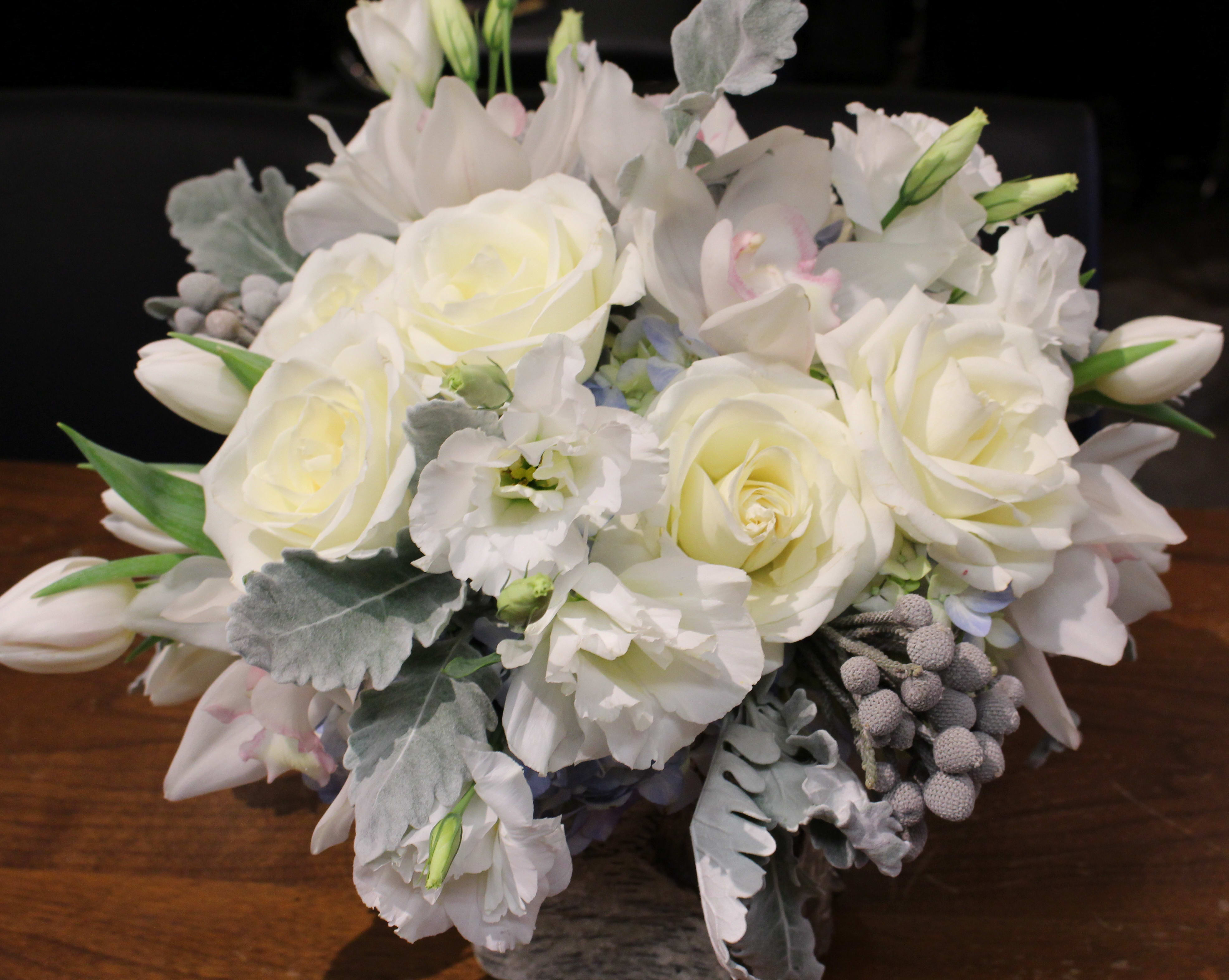 Winter Bliss - A Beautifully Hand Crafted Floral Design Consisting of a Color pallets of Blues, Whites, Creme, with natural accents Silver Burnia, and Dusty Miller Leaves arranged in a nautral birch bark container. Prefect to Enhance any Coffee or Dining Room Table this holiday season 