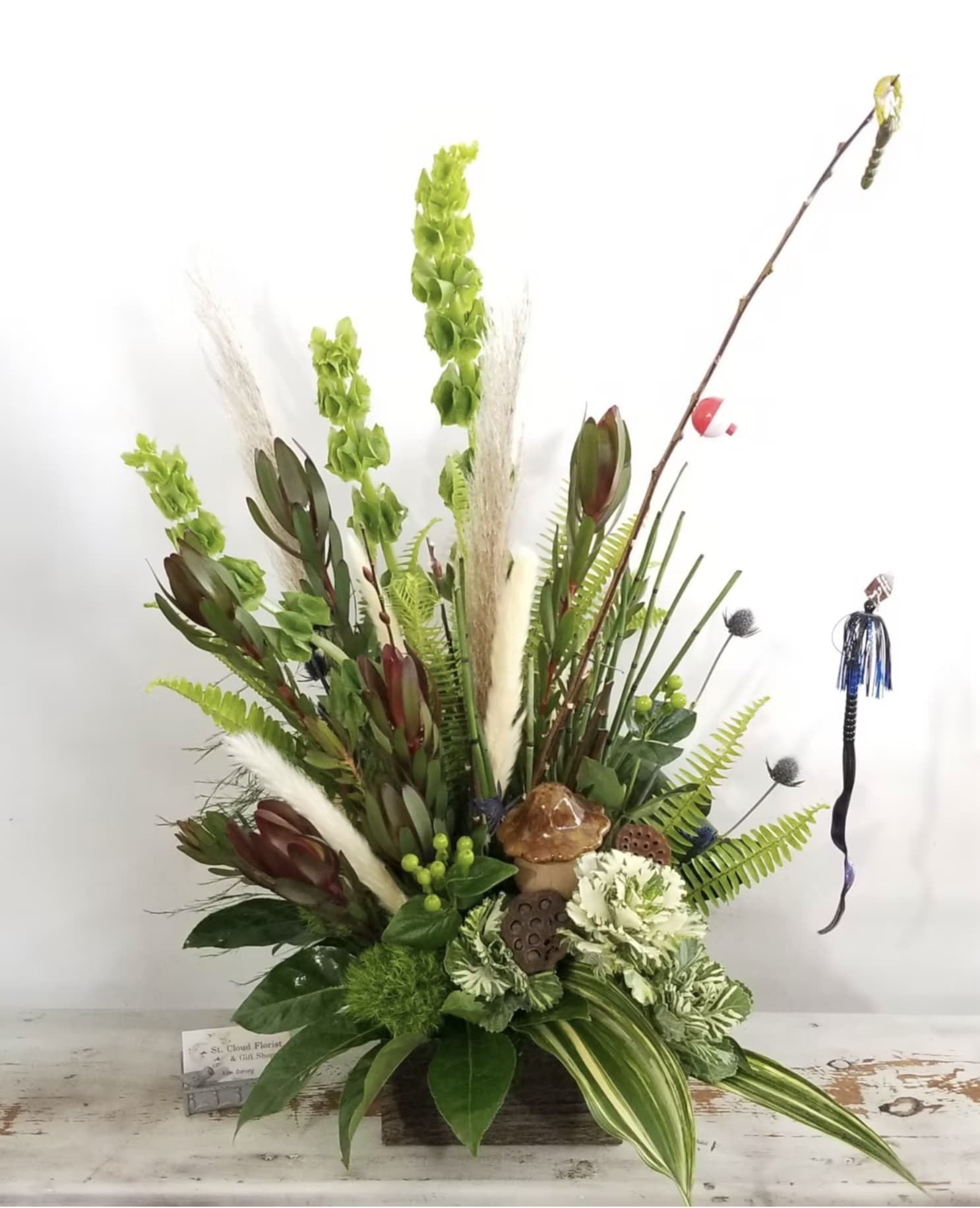 Custom Woodsy Arrangement W/Fishing Pole - Flowers and containers are subject to substitution and availability. Fishing pole accessories and gift item are subject to designers choice at time of design.