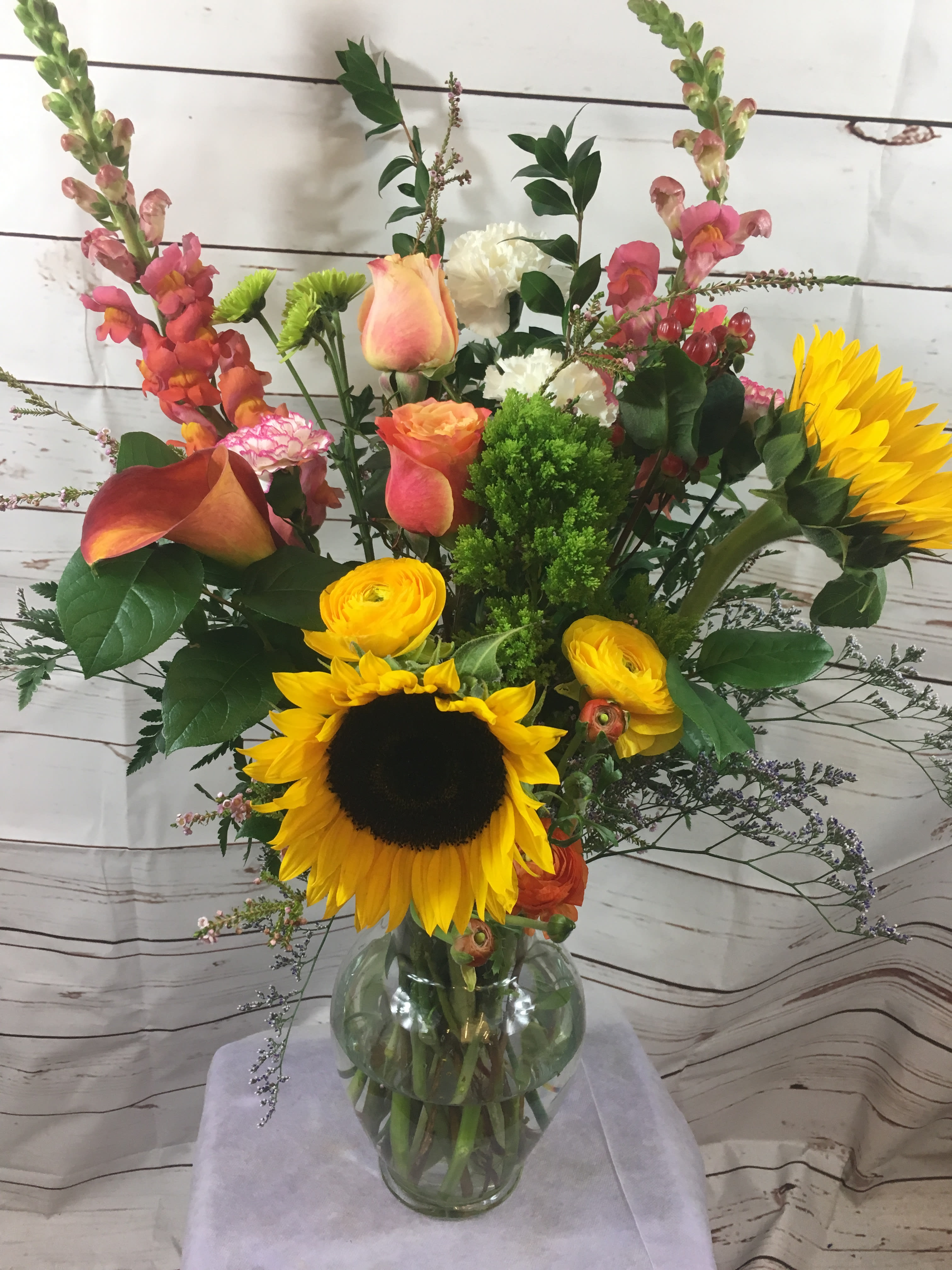 Bright and joyous by Seulberger's Florist - A cheerful and upscale floral arrangement of sunflowers,ranunculus,snapdragons,exotic colored calla lilies,hypericum berries,tulips and roses will brighten the spirit and surely the mood wherever it goes.