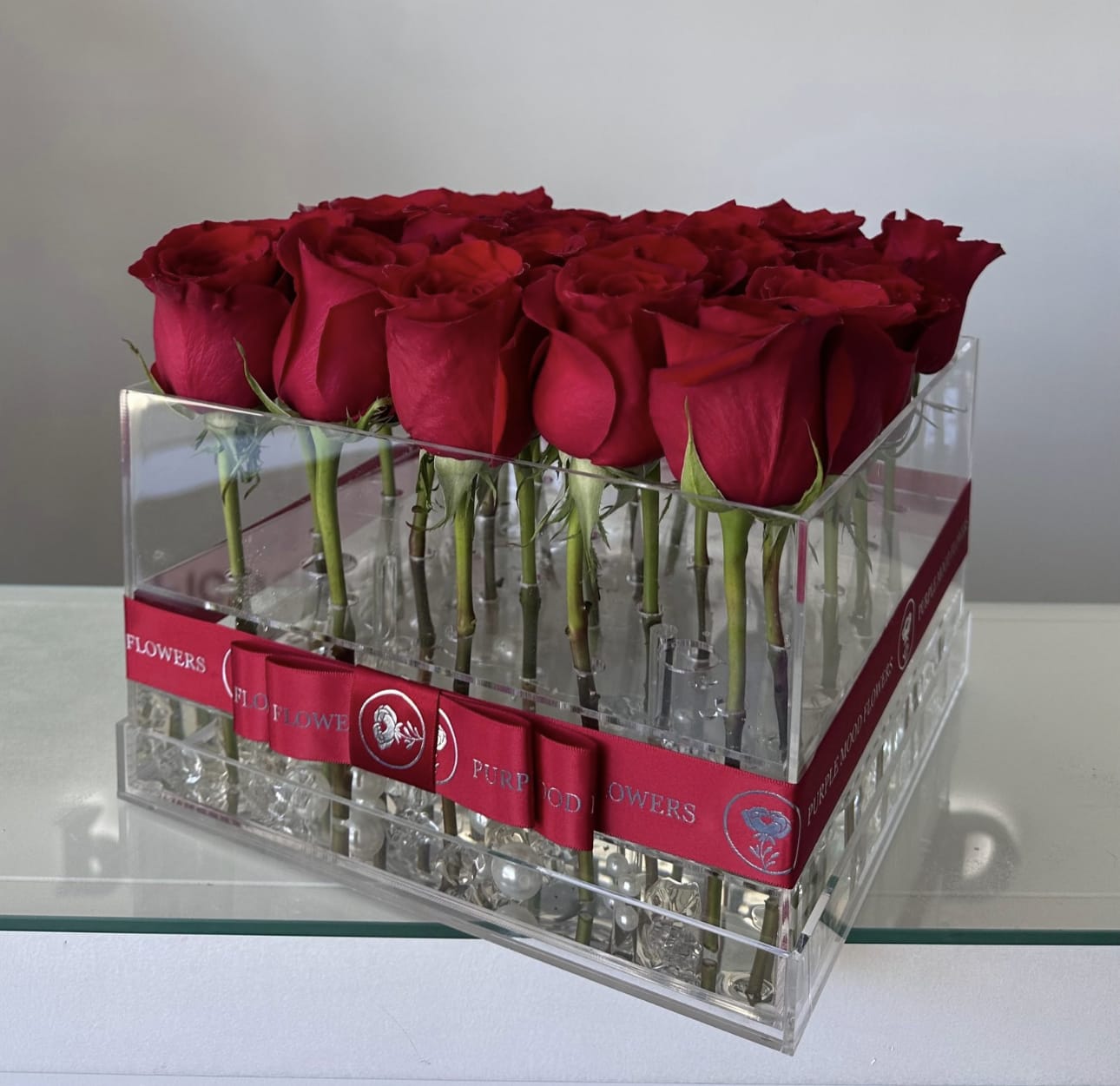 Acrylic Box - 25 roses in an acrylic box. Modern, sleek, and unforgettable — our Acrylic Box Roses arrangement showcases premium roses in a crystal-clear acrylic case. This chic design blends elegance with contemporary style, allowing each rose to stand tall and shine beautifully. Perfect for someone who loves a modern twist on a timeless classic, this arrangement is a stunning gift for anniversaries, romantic gestures, or stylish celebrations.   •    Premium roses displayed in a clear acrylic box     •    Modern design that keeps each stem in perfect position     •    Elegant and long-lasting presentation with minimal maintenance     •    Ideal for anniversaries, Valentine’s Day, or contemporary-style gifting