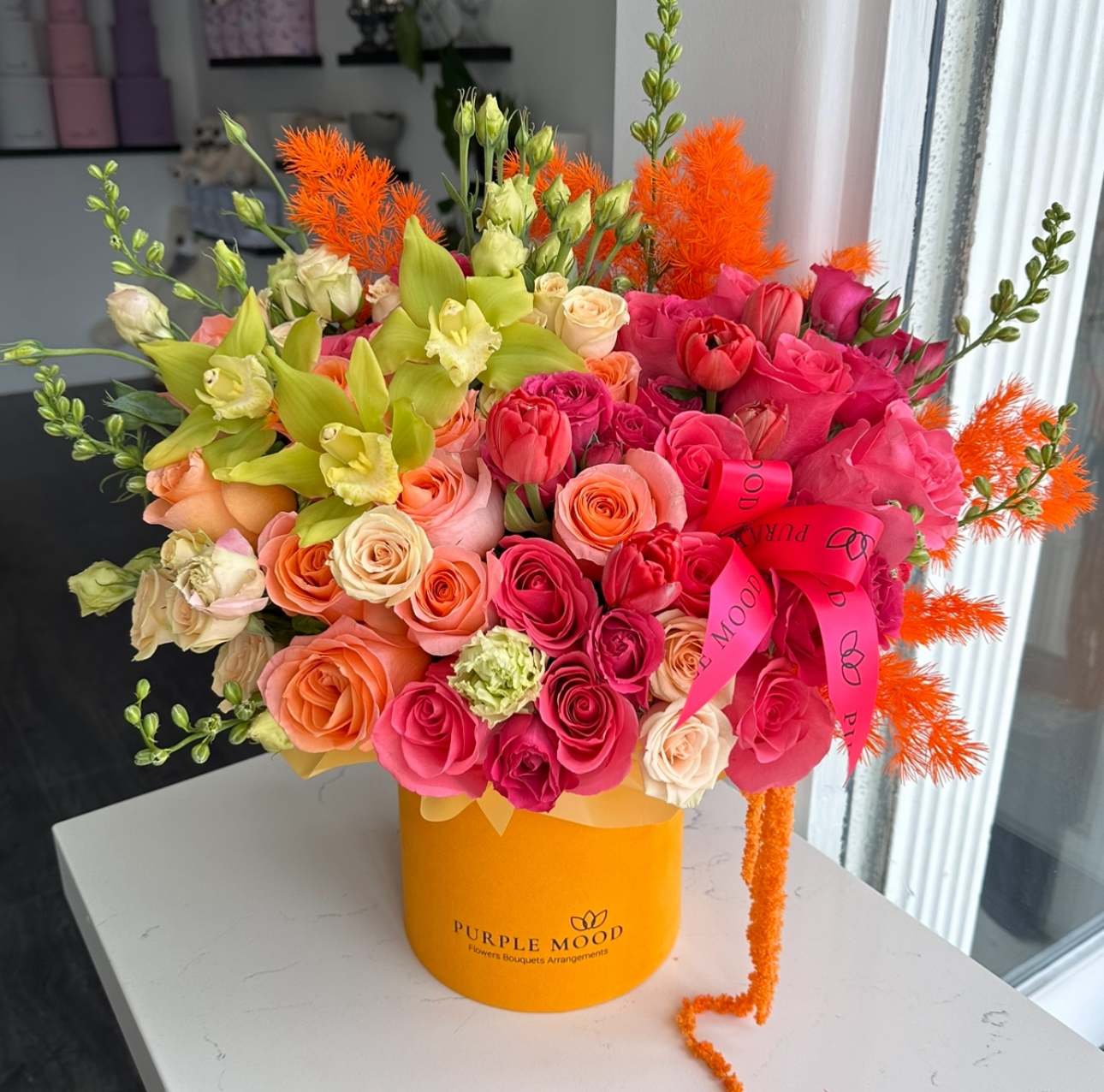 Sweet Mango Box - Container size - D6.75'x H7.5'  Sweet Mango Box Bring the warmth of sunshine into any space with the Sweet Mango Box. Bursting with juicy shades of orange, coral, pink, and yellow, this cheerful arrangement radiates positivity and joy. Designed in our signature velvet box, it’s the perfect gift to brighten someone’s day and leave a lasting impression.      •    Bright and vibrant mix of warm, sunny colors     •    Arranged in our signature velvet box     •    Bold yet playful design full of happiness     •    Ideal for birthdays, celebrations, or simply sending joy