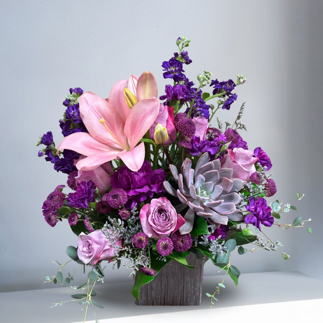Love Like This - The color purple is often associated with royalty, nobility, luxury, power, and ambition. Purple also represents extravagance, grandeur, devotion, mystery, independence, and magic.  Recipe: Pink Lilies, Purple Stock, Carnations, Buttons, Lavender Roses, and Succulent in a silver, square vase. Seasonal: All year round Orientation: Front Facing View Photo shown: Standard 
