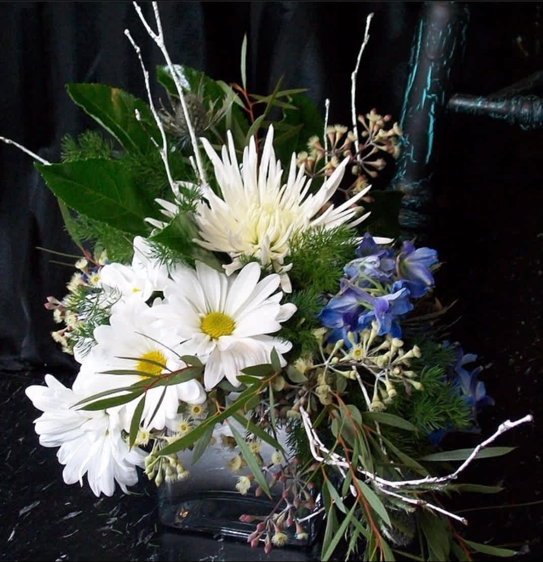 Winter Greetings.  A Floral Archist™ original. -  A bright and organic member of our ‘Winter Celebration Collection’.  This beautiful custom designed floral piece is the perfect way to wish your loved ones a beginning for this blessed season and a prosperous new year!  As with ALL our designs, selection of blooms vary with each Upgrade. As part of our Winter Celebration Collection, this design serves ALL winter celebrations.   Psst! Guys would love to receive flowers too!   NOTE: Our flowers and greens are a gift from nature. It’s shade and depth might vary, design, aesthetic and value remains the same. In support of our efforts to aide in the preservation of our planet, PJf uses Fair Trade flowers, Plants, Upcycled and Recycled containers.