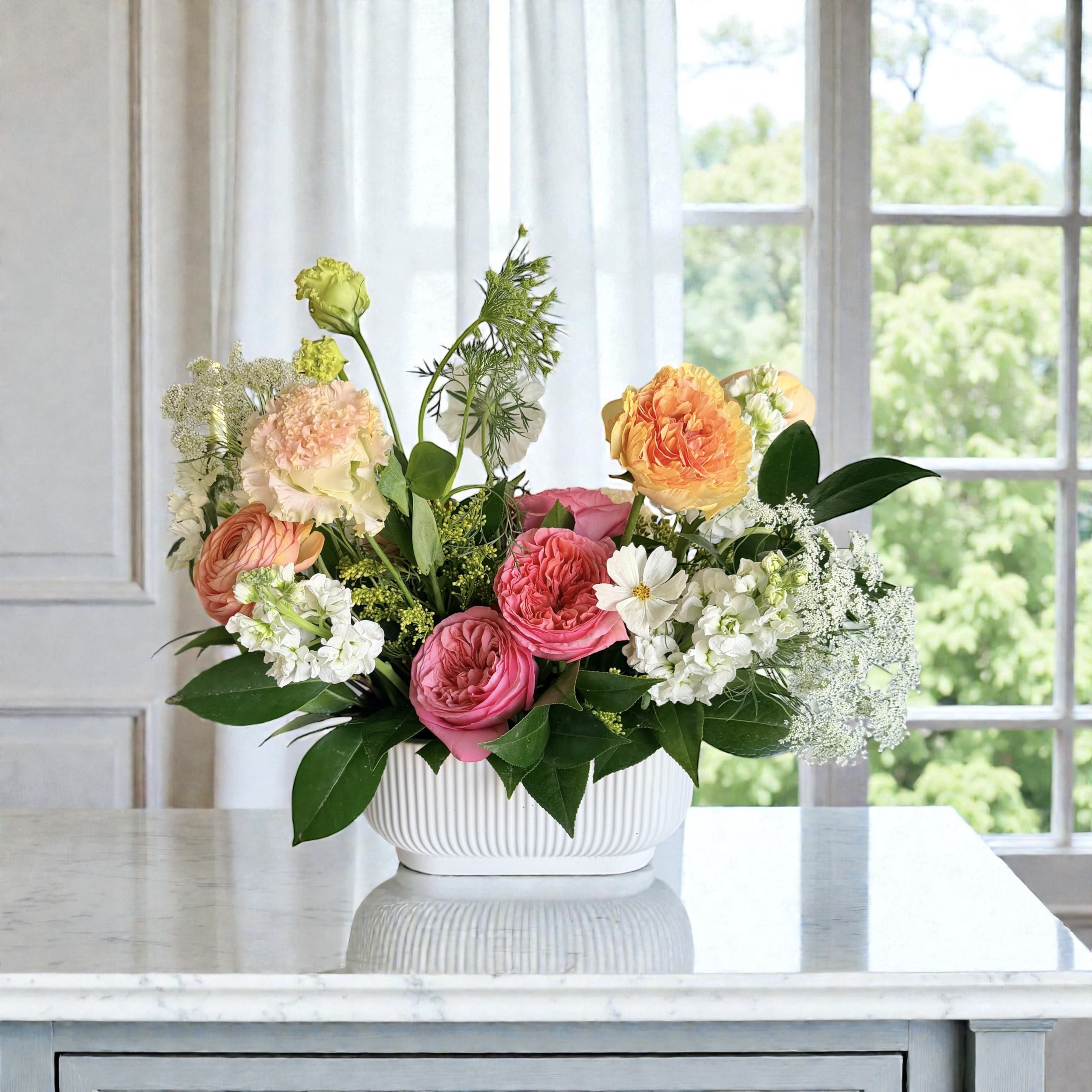 Blushing blooms - A fresh, garden-inspired arrangement designed with a soft, airy feel. Roses , ranunuclus alongside delicate chamomile, tulips, and seasonal wildflowers, all nestled in a modern ceramic vessel. Light, romantic, and naturally elegant — perfect for brightening a home, sending a gentle thank-you, or celebrating life’s everyday moments.  For same day delivery call us at 9496825004