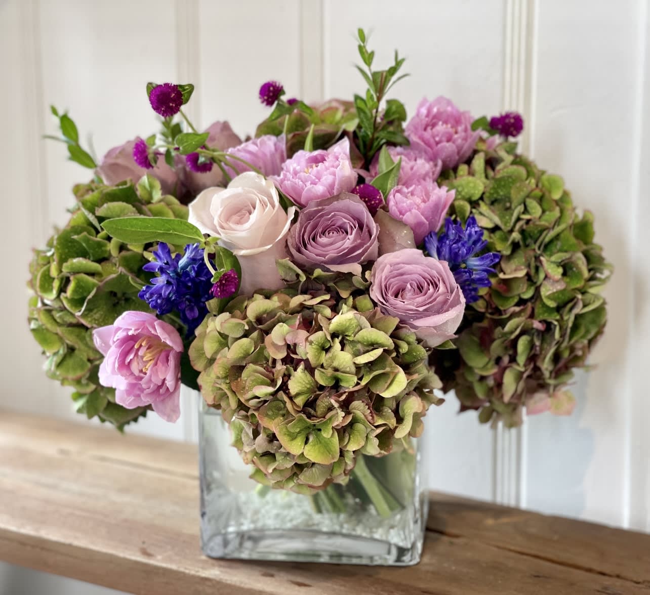SPECIAL TO ME - A well balanced beautiful design of soft and deeper purple roses, paired with the most gorgeous double purple tulips, and stunning antique green/ purple hydrangeas. This one comes designed in a 6x6 square glass container.