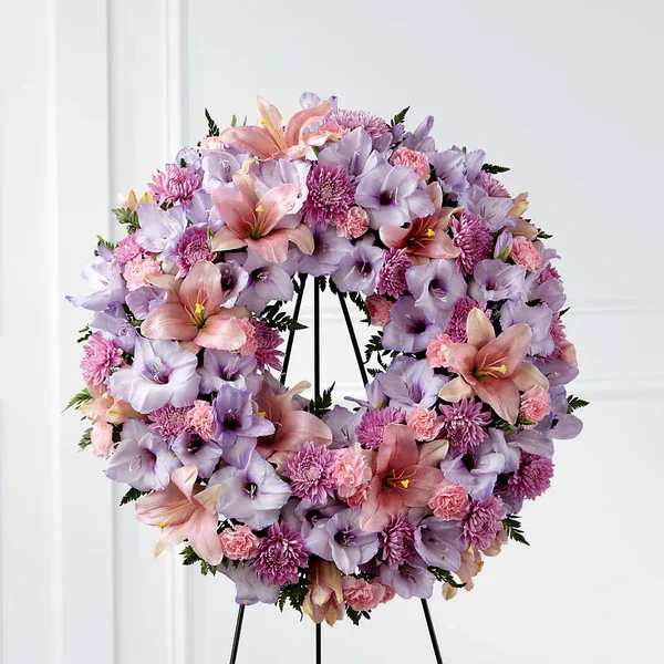 Beloved Friend Wreath - Our Beloved Friend Wreath beautifully honors a life that was cherished by so many. This classic arrangement stands tall with an array of lilies, gladiolus and carnations in lavender and pink shades to express your love for the friends who truly feel like family.  The picture you see is only the design of each product. Every and each one can be made in the 3 sizes that we have. The deluxe is 24 inches. The premium is 28 inches. The Exquisite is 32 inches. These measures are only for the funeral wreaths. Please make sure to read the measures of each size. The picture reflected in these products is the premium one  Please Note: The bouquet pictured reflects our original design for this product. While we always try to follow the color palette, we may replace stems to deliver the freshest wreath possible, and we may sometimes need to use a different vase.