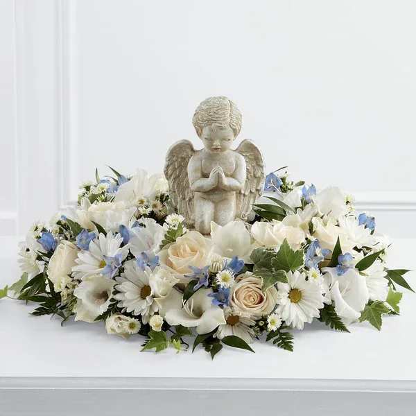 Little Angel Ring of Flowers - The Little Angel Ring of Flowers is a sweet and serene way to say your final goodbye at a child's final farewell service. A stonecast cherub statue sits in the center of a ring of white roses, white traditional daisies, white monte casino asters, light blue delphinium, white gladiolus and a variety of lush greens to create a beautiful tribute that expresses your unending love and affection for the deceased.  Please Note: The bouquet pictured reflects our original design for this product. While we always try to follow the color palette, we may replace stems to deliver the freshest bouquet possible, and we may sometimes need to use a different vase.