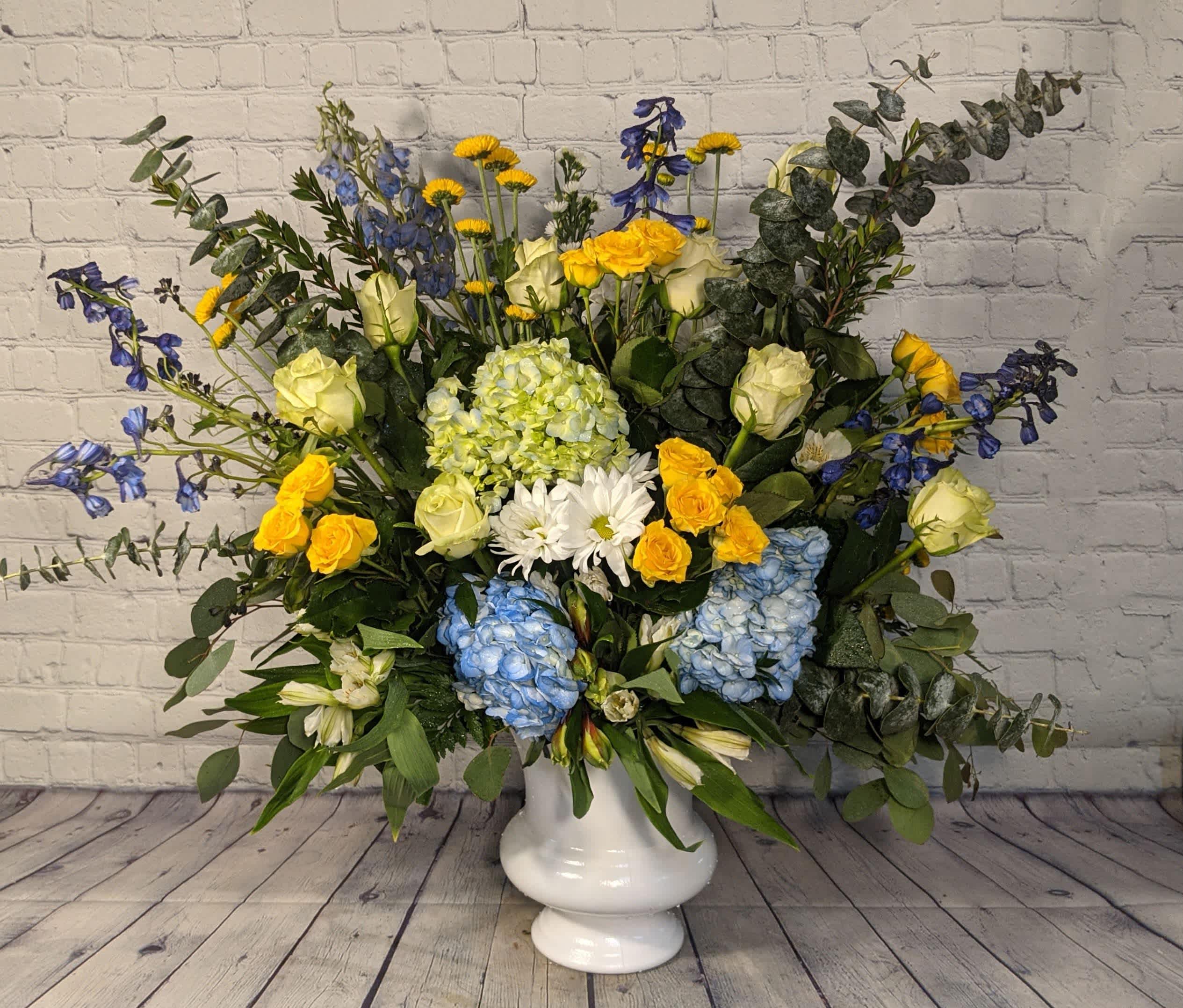 Timeless Blues - This elegant urn piece will be the perfect selection for either your thoughts of condolence or your treasured memories. From its deep blue delphinium to its delicate white roses, yellow spray roses, eucalyptus, and stock; our "Timeless Blues" arrangement beautifully conveys your heartfelt sympathy.