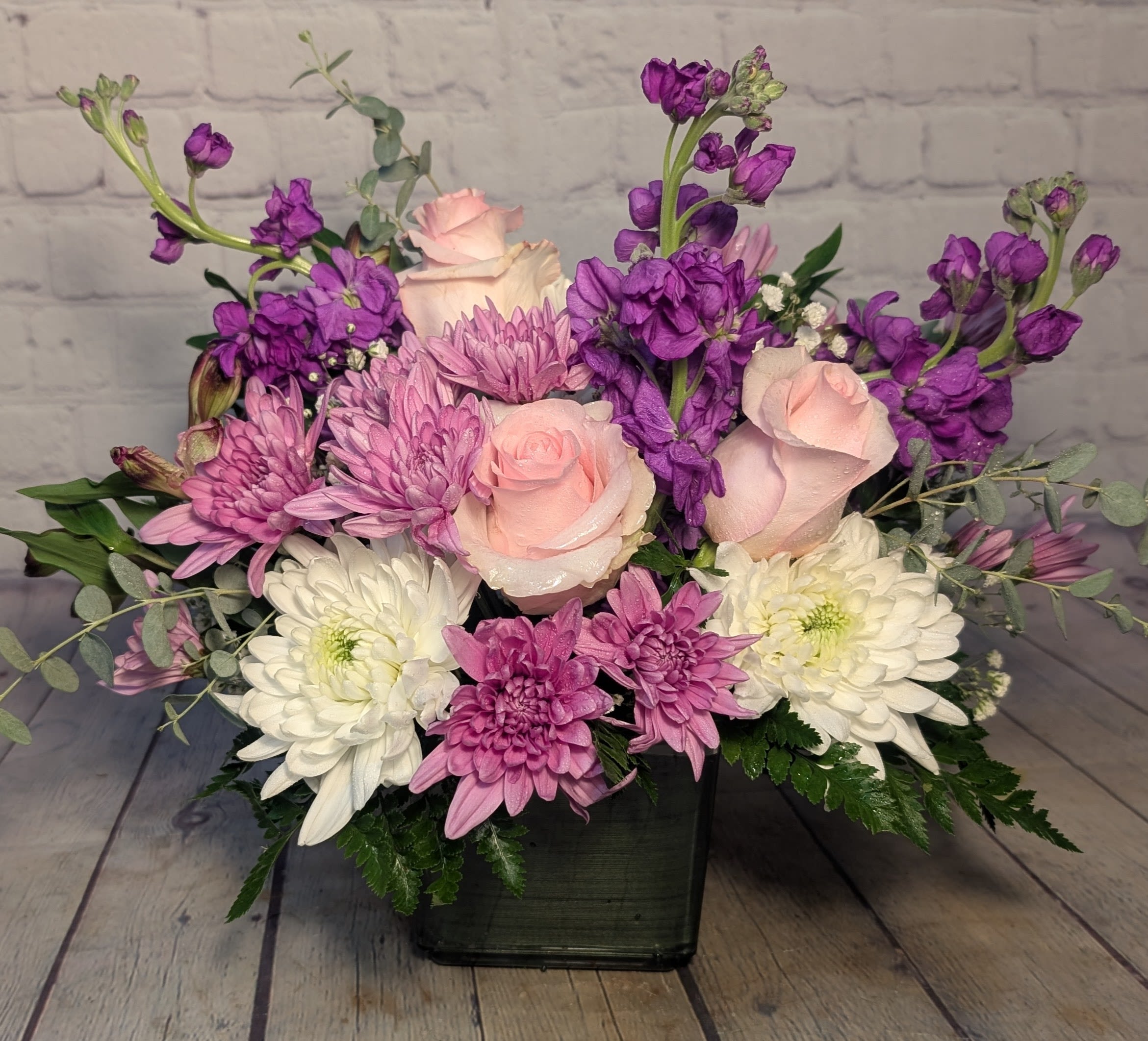 Lavender Bliss - Soft, sweet, and effortlessly elegant — Lavender Bliss is a dreamy mix of pink roses, white fuji mums, lavender stock, lavender chrysanthemums, and delicate filler blooms in shades of white and lavender. Arranged in a modern cube vase, this bouquet exudes serenity and charm, making it perfect for any occasion that calls for a touch of beauty and grace.