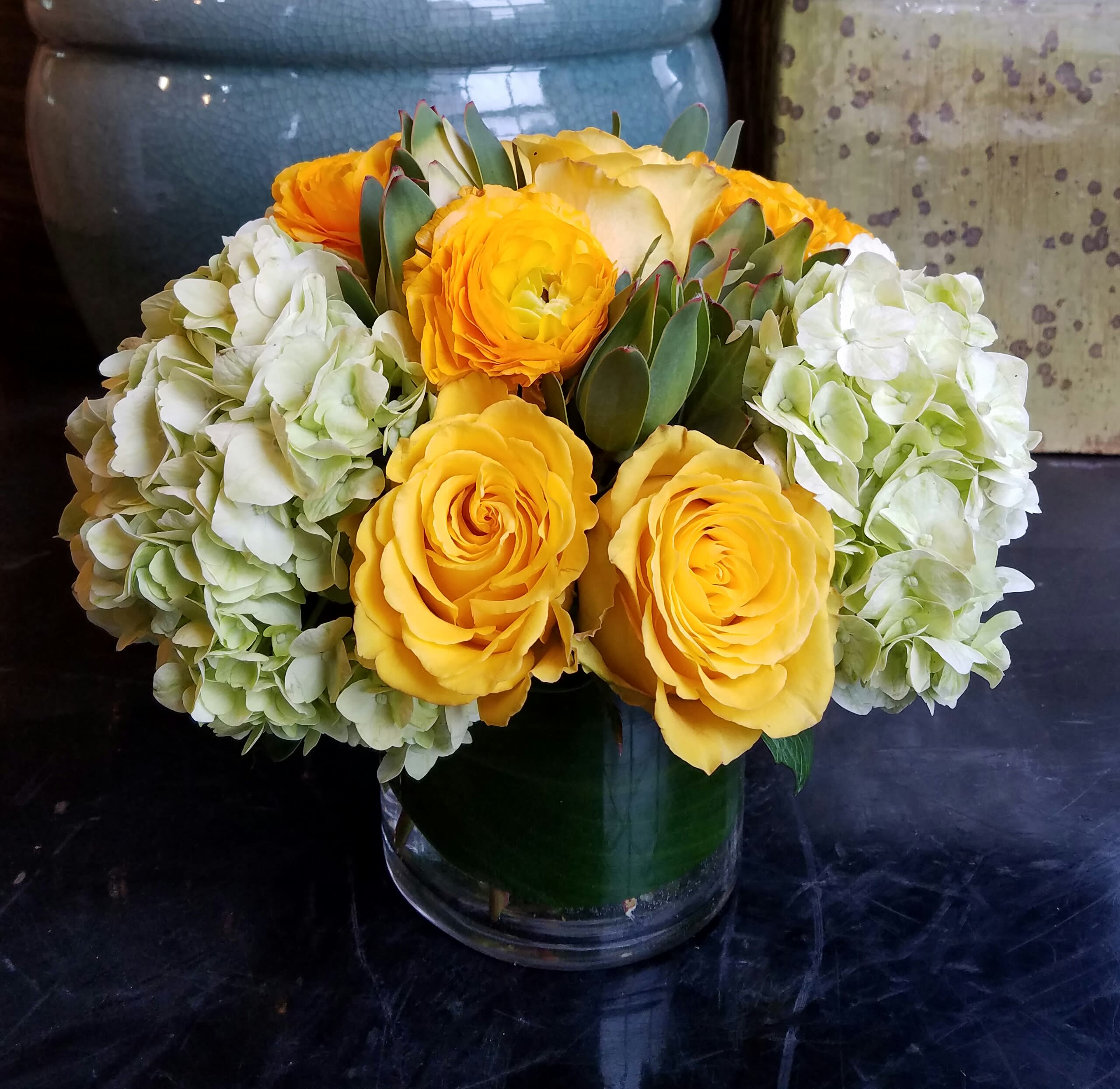 Yellow Submarine - We all lived in a yellow submarine...!  This bright and sunny arrangement features yellow Roses, Ranunculus and Mojito Hydrangea with complementary blooms in a leaf wrapped glass cylinder. Ahoy matey's!