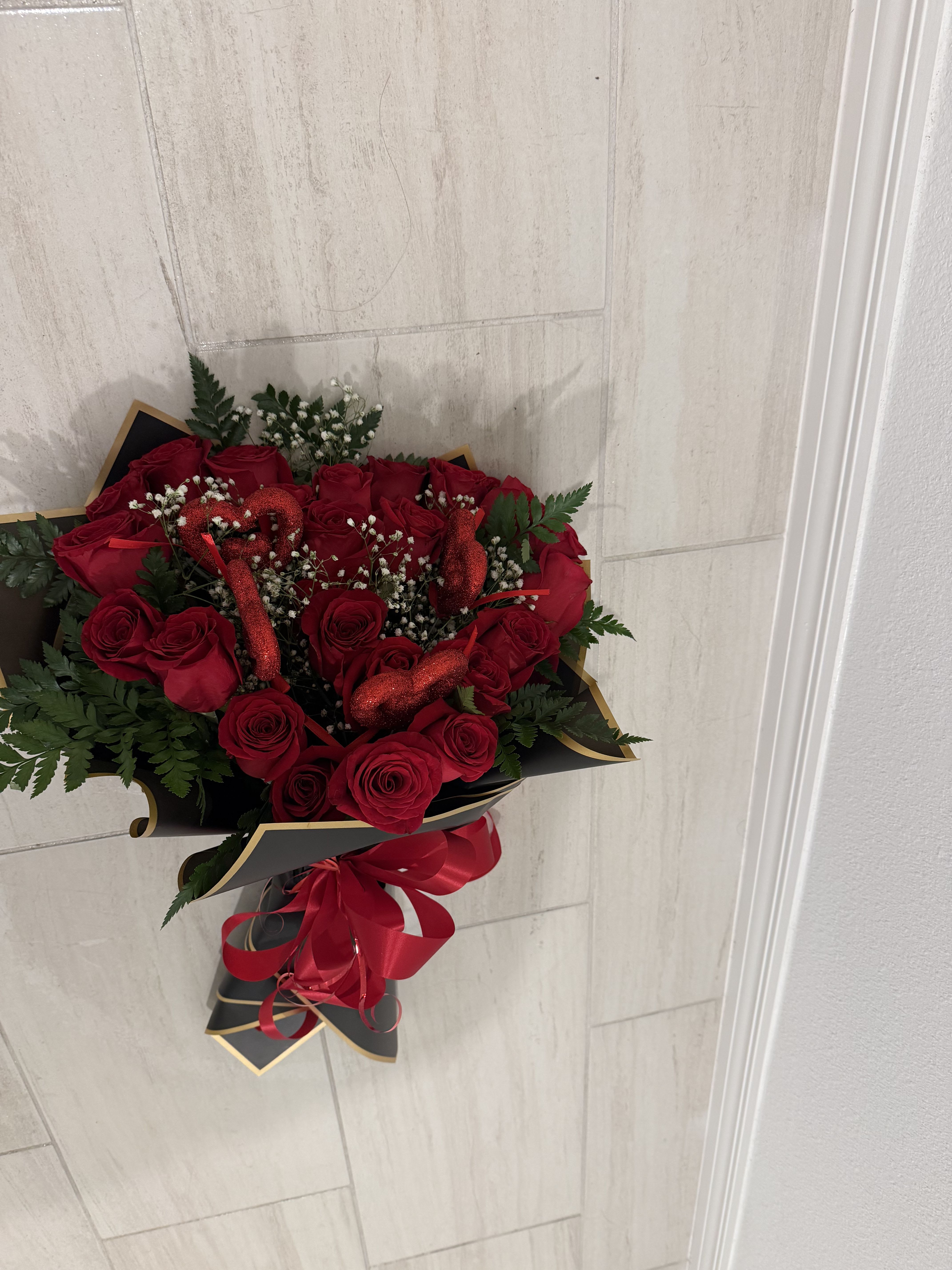 Two Dozen Eternal Love - stunning bouquet of 24 premium red roses, beautifully wrapped in elegant black and gold paper. Accented with delicate baby’s breath, lush greenery, and sparkling red glitter heart picks, this arrangement radiates passion and romance. Finished with a luxurious red ribbon, it’s the perfect gift to celebrate love, anniversaries, Valentine’s Day, or any unforgettable moment.