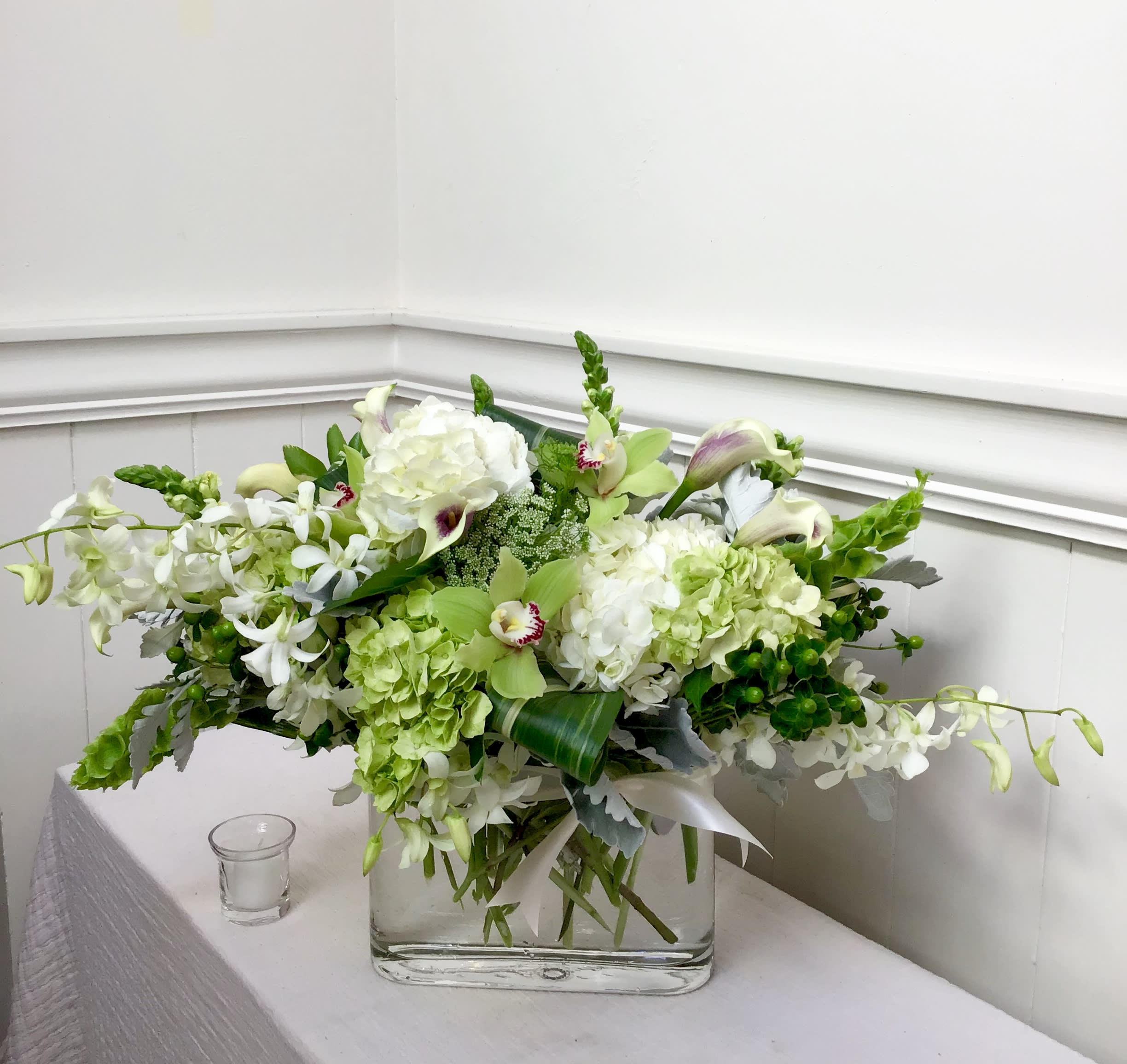 Layers of Luxury - An elegant oval clear glass vase, arranged with premium white and green flowers. Including calla lilies, hydrangea and dendrobium and cymbidium orchids.