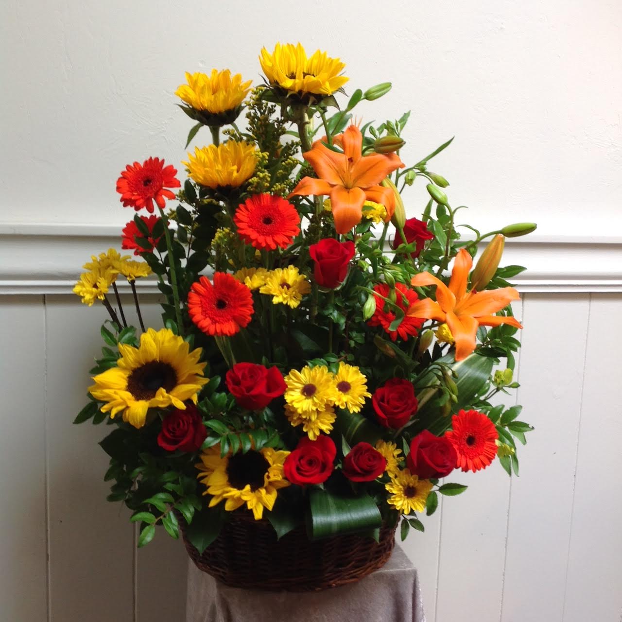 Rover - This dark basket is filled with orange lilies, gerbera daisies, sunflowers and red roses. This piece is tall and full, beautiful for a memorial service.