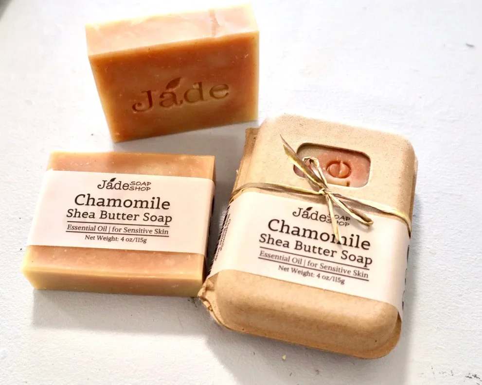 Chamomile Shea Butter Soap - Chamomile Shea Butter Soap -  handmade by our artisan partners @ Jade Soap Shop  Made with: Saponified Olive Oil, Coconut Oil, RSPO Palm Oil, Shea Butter. Chamomile Powder, Madder Root Powder. Natural Chamomile F.O., Lavender E.O. ** Jade Soap Shop uses Sodium hydroxide for saponification. There's no sodium hydroxide exits in the soap after the saponification is done.*** Fun Facts of Key Ingredients: Chamomile is one of the best skincare herbs available and is particularly useful for skin conditions such as contact dermatitis (eczema). This apple-scented herb comes in several different forms, but thankfully they all offer natural beauty benefits. Chamomile is antibacterial, anti-fungal, anti-inflammatory and antiseptic. Shea Butter has such a large healing fraction, in addition to moisturizing fraction, regular use of this natural cream can treat many skin problems, including blemishes, wrinkles, itching, sunburns, small skin wounds, eczema, skin allergies, insect bites, frostbite, and other skin conditions.  Use For: Body Wash. Weight: Full Size Bar approx. 4 oz/shrink wrapped 
