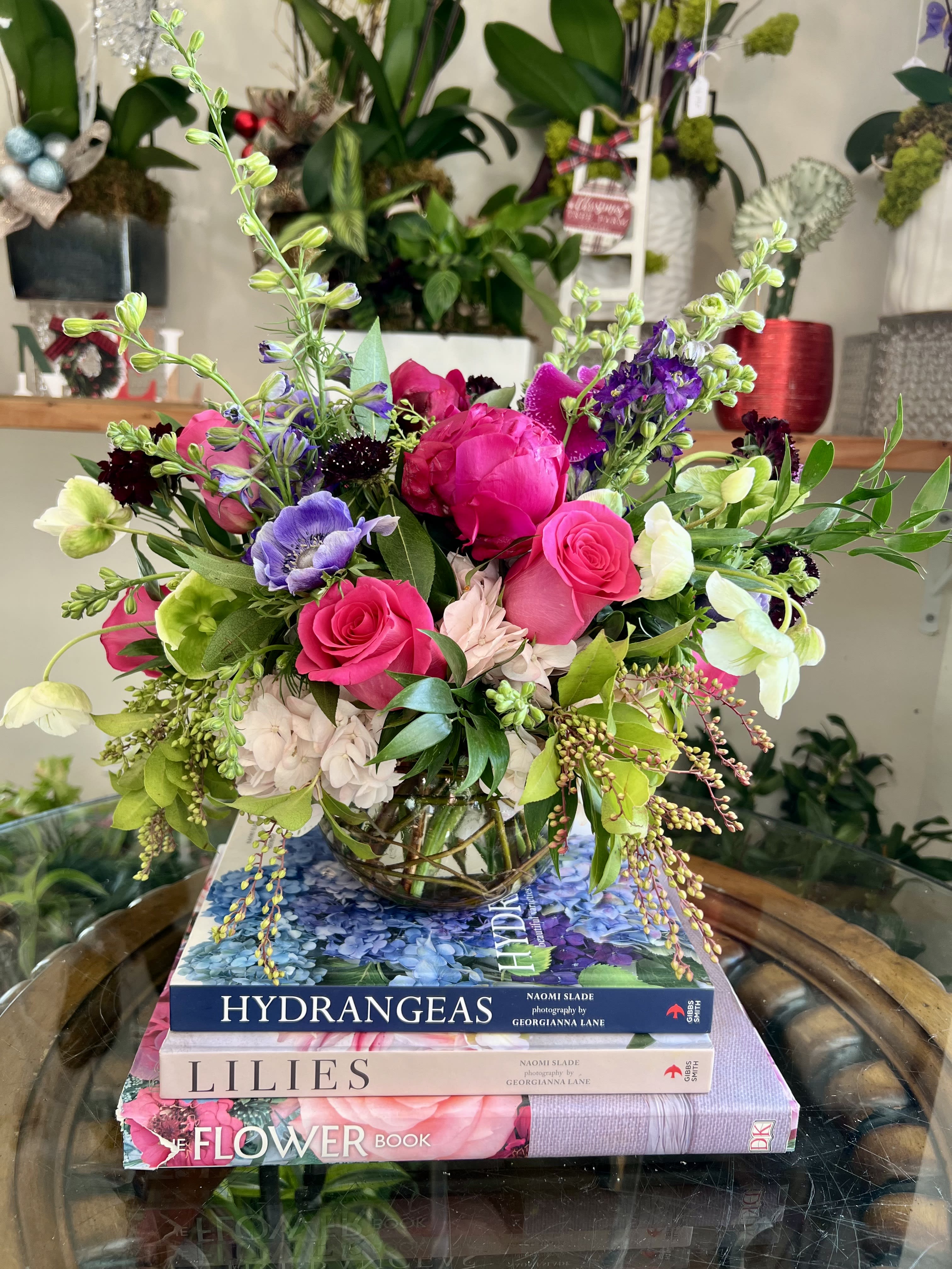 Dragonfruit Infusion - Vibrant, playful, and effortlessly chic, the Dragon Fruit Infusion arrangement dazzles with a palette of hot pinks, blush, and rich purples. Designed in a small fishbowl vase artfully lined with curly willow. Light pink hydrangeas create a soft, cloud-like base, while Pink Floyd roses &amp; peonies add a bold pop of fuchsia. Striking purple anemones, phalaenopsis orchids, and delicate purple larkspur bring moody elegance, complemented by airy scabiosas and hellebores.  Seasonal greenery adding fresh movement and balance.  Perfect for adding a splash of modern sophistication to any space, this arrangement is as bold and refreshing as its namesake fruit—a true statement piece bursting with color and style.